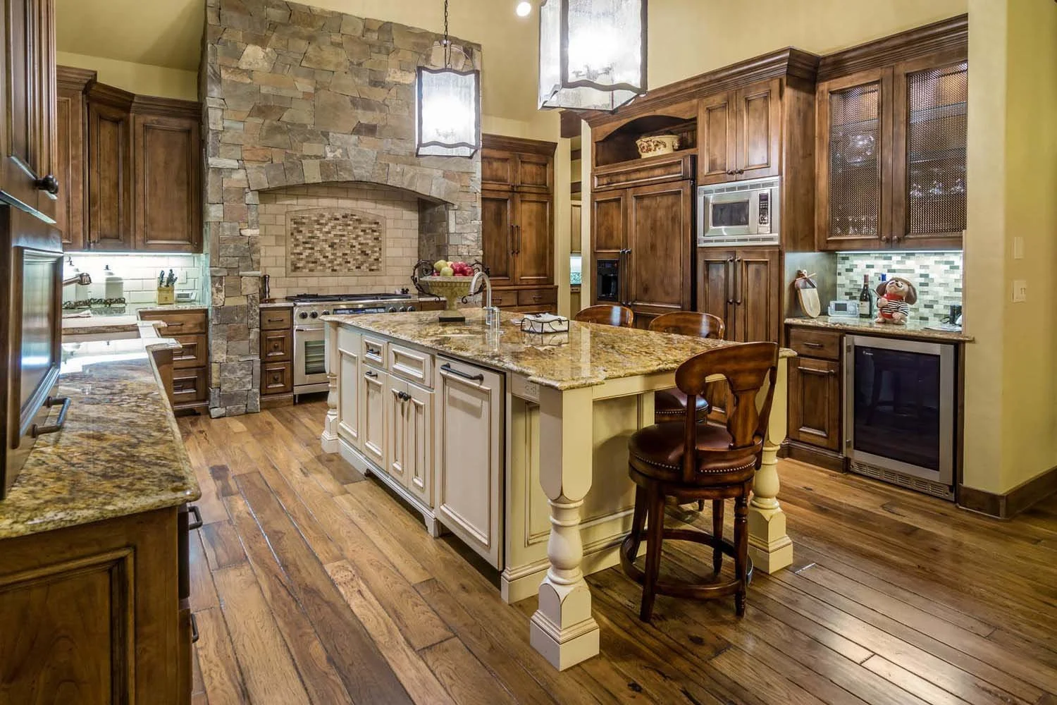 This spacious kitchen, a 2017 COBA Tour winner for "Best Kitchen," is a highlight of a luxury custom home in Caldera Springs - Trailmere Circle. The space features a large island with a granite countertop, wooden floors, and a stunning stone wall wit