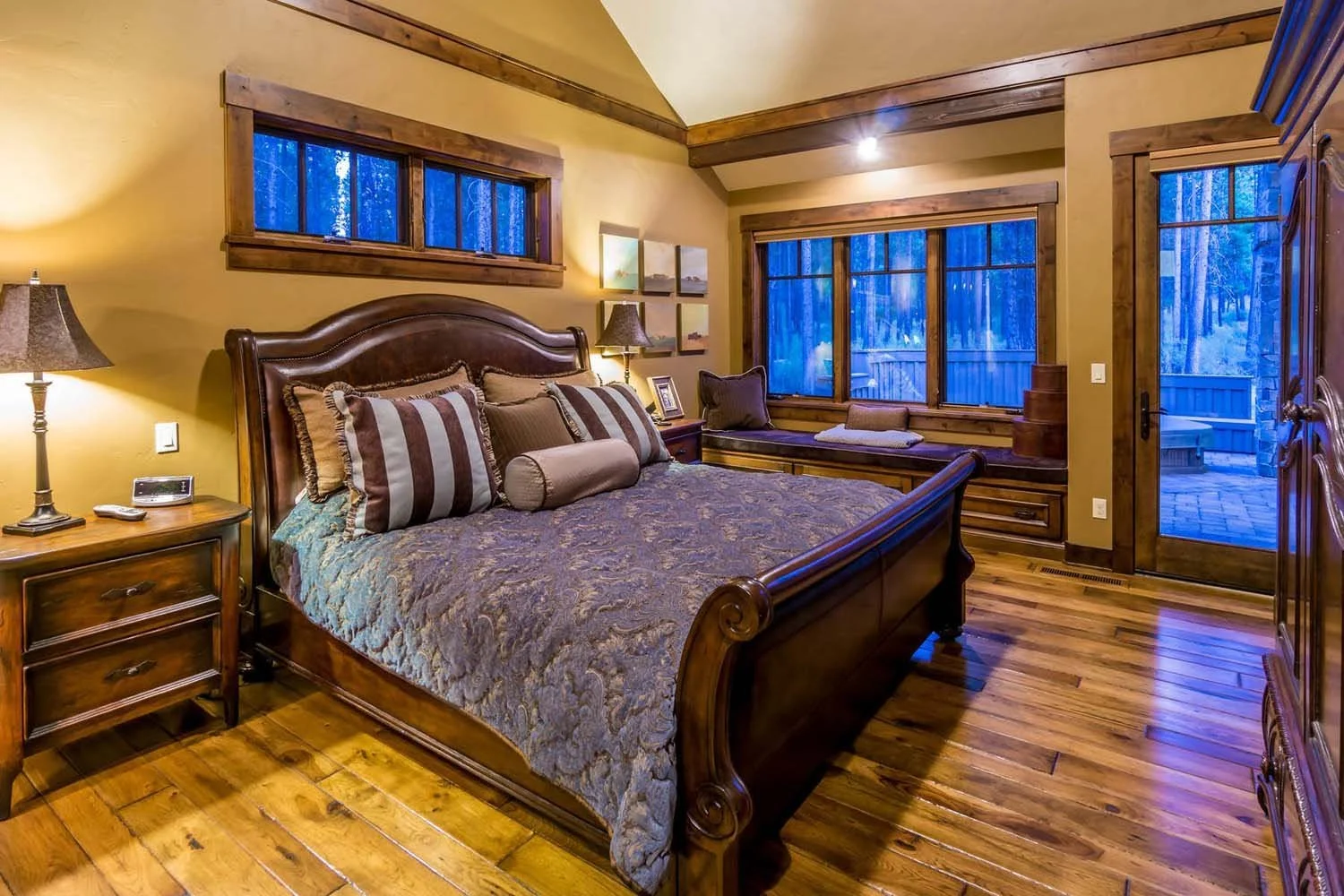 This cozy bedroom, a key feature of a luxury custom home in Caldera Springs - Trailmere Circle, showcases masterful interior design by Kristy Yozamp. The space, with its large wooden bed and warm yellow walls, creates a welcoming atmosphere. The wind