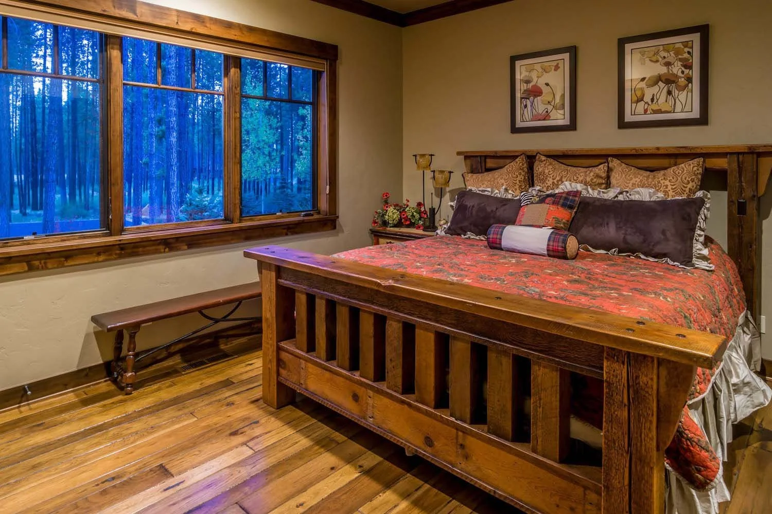 This cozy bedroom in Caldera Springs - Trailmere Circle is a showcase of impeccable interior design by Kristy Yozamp. The space, with its wooden bed frame, patterned bedding, and beautiful flower artwork, creates a warm and inviting atmosphere. The l