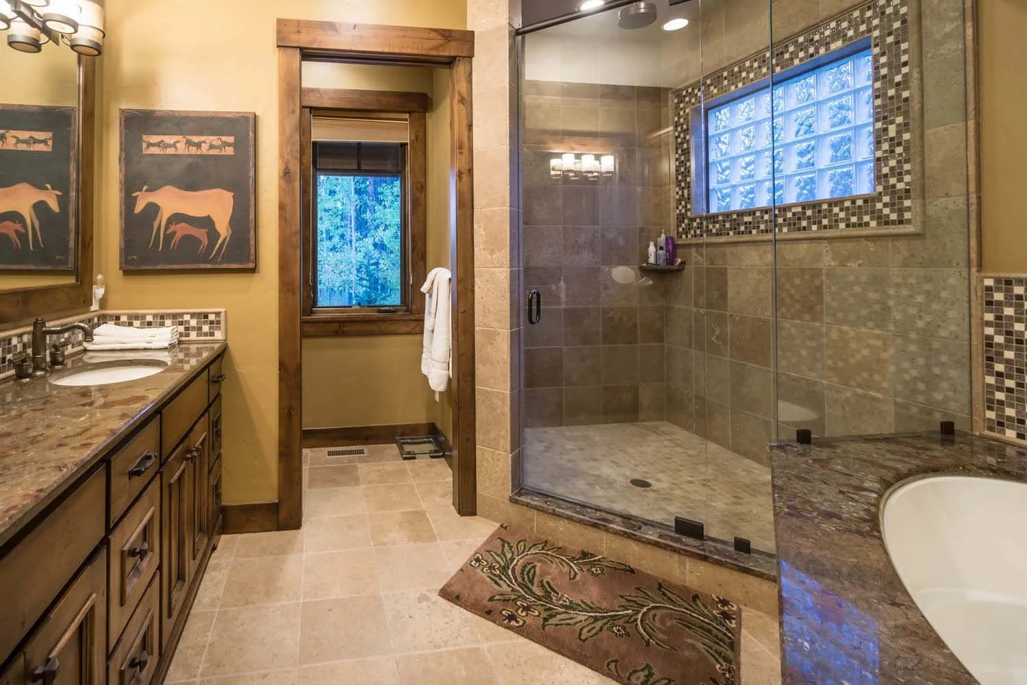 This bathroom, a key feature of a luxury custom home in Caldera Springs - Trailmere Circle, showcases masterful interior design by Kristy Yozamp. The space features a beautiful wooden-framed window, a shower with glass doors, and a granite-topped van