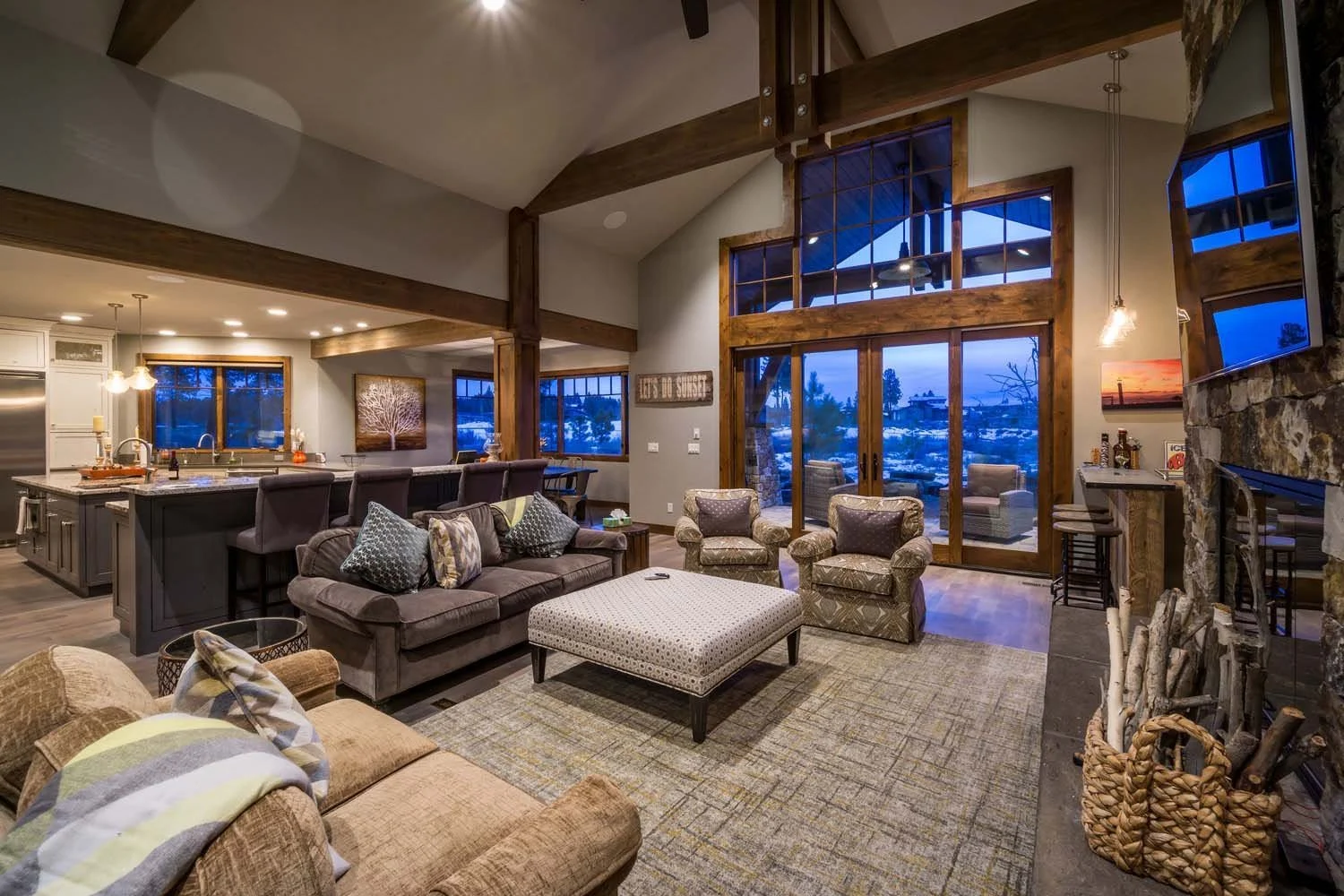 This living room, a key feature of a luxury custom home in Tetherow - Hosmer Lake Drive, showcases masterful interior design by Kelly Warner. The space features a stone fireplace, cozy chairs, and a sectional sofa, creating a comfortable and inviting