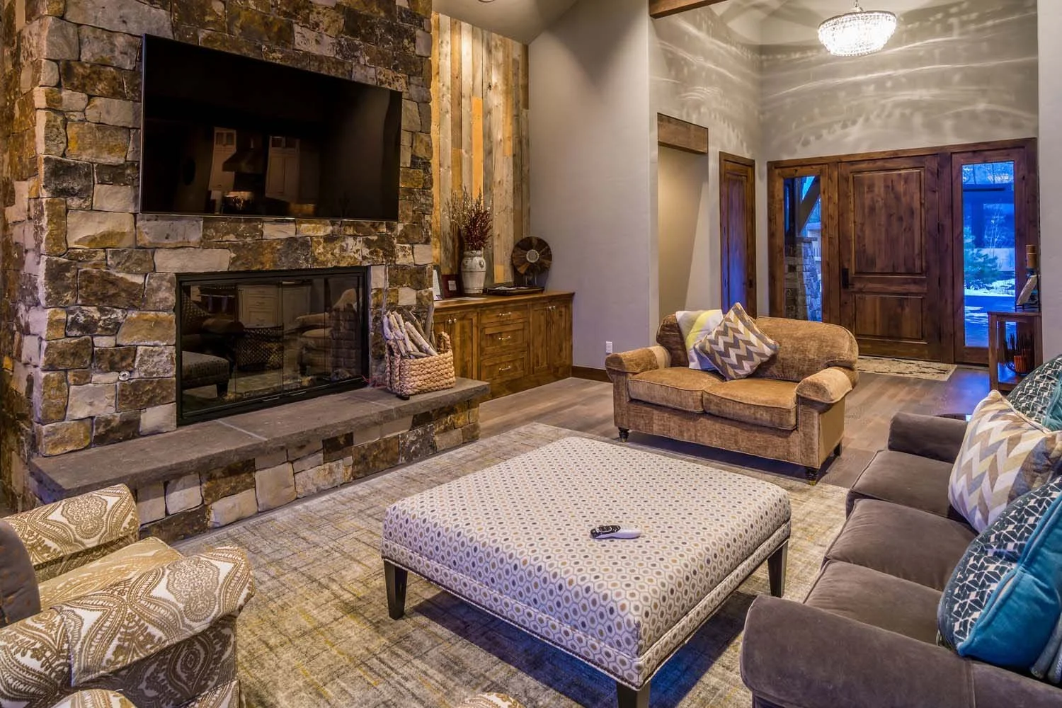 This mountain modern living room, a key feature of a luxury custom home in Tetherow - Hosmer Lake Drive, showcases masterful interior design by Kelly Warner. The space, which has the feel of a mountain lodge, features a stone fireplace, a mounted fla