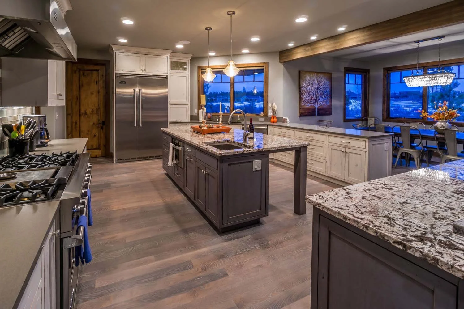 This exceptional kitchen in Tetherow - Hosmer Lake Drive, a luxury custom home, is a testament to the masterful interior design by Kelly Warner. The space features granite countertops, a central island, and stainless steel appliances, all perfectly b
