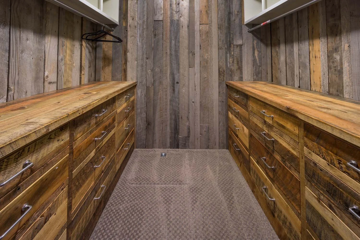 This rustic walk-in closet in Tetherow - Hosmer Lake Drive is a testament to the masterful interior design by Kelly Warner. The space, which has the feel of a mountain lodge, features beautiful wooden drawers and wood-paneled walls, all reflecting th
