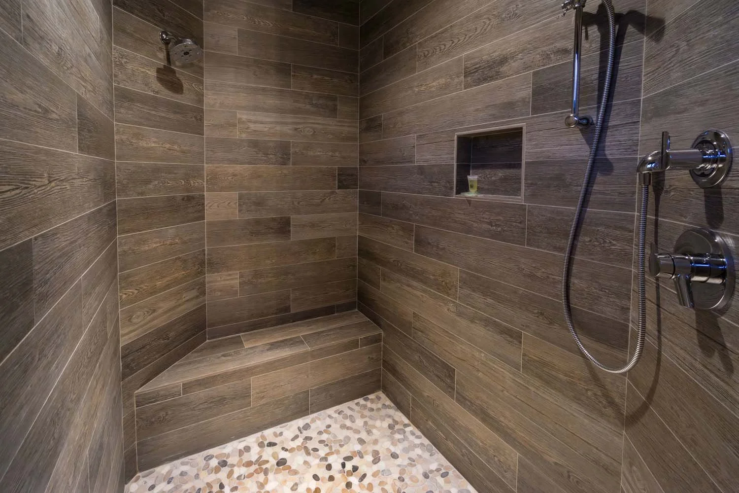 This luxurious modern walk-in shower in Tetherow - Hosmer Lake Drive is a testament to the masterful interior design by Kelly Warner. The space features wood-look tile walls, a built-in corner bench, and pebble tile flooring, perfectly blending natu