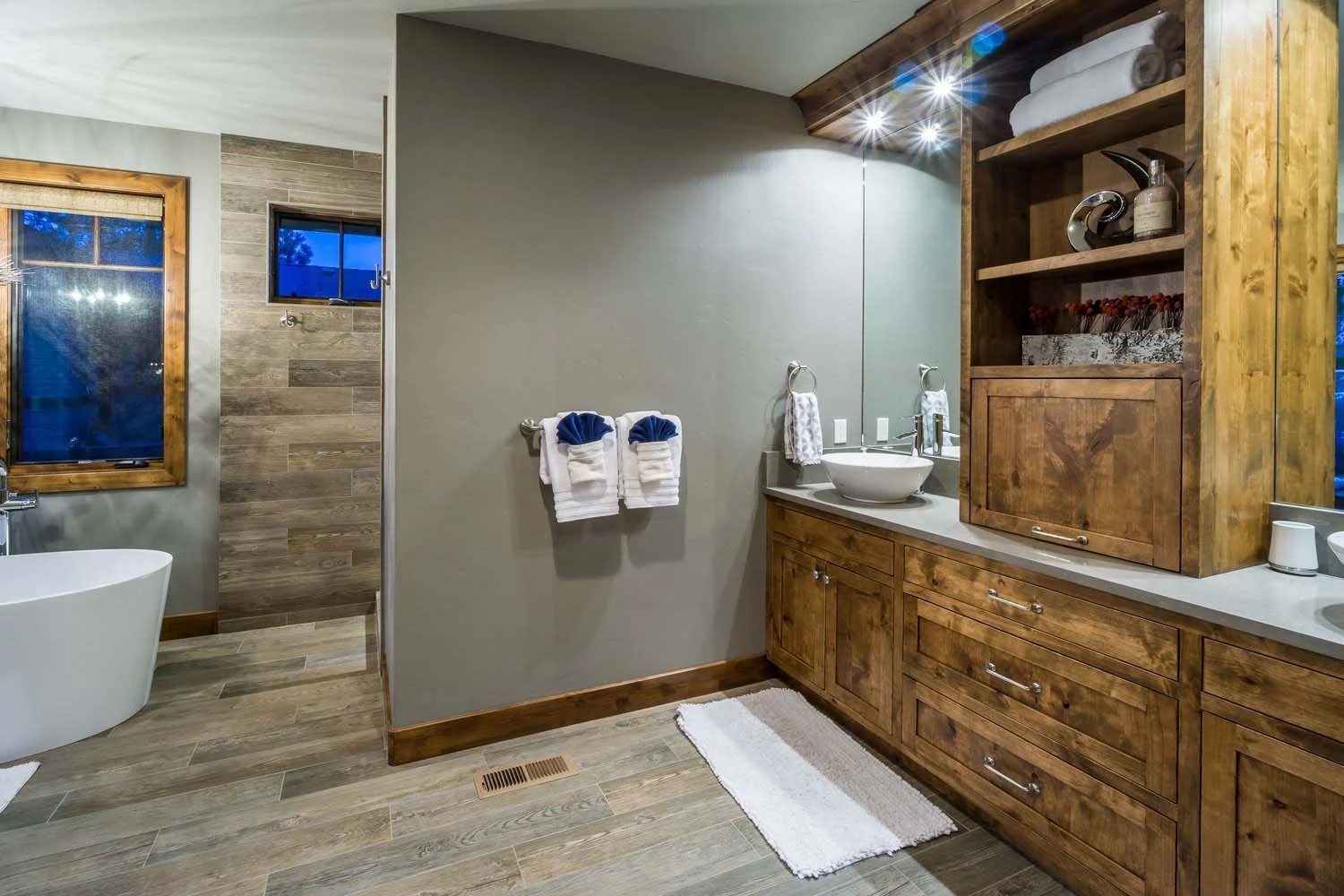 This modern bathroom in Tetherow - Hosmer Lake Drive, a luxury custom home, showcases the masterful interior design by Kelly Warner. The space features a wooden vanity with a vessel sink, a mirror, and a bathtub, perfectly blending modern and rustic
