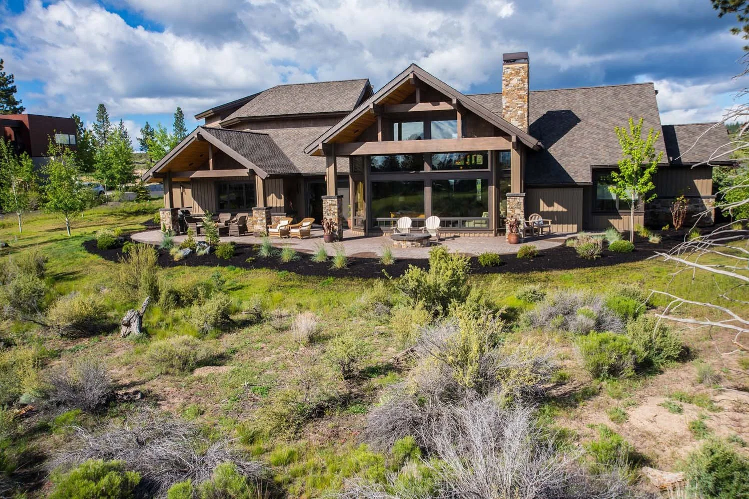 This luxury custom home in Tetherow - Weinhard Court, designed by Spencer Williams, is a masterpiece of modern architecture. The house features a large patio and is surrounded by a beautifully landscaped garden and trees, blending seamlessly with the