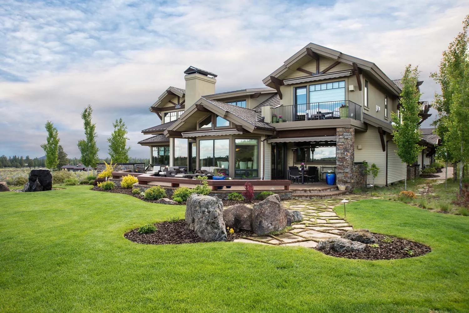 This luxury custom home in Tetherow - Skene Trail, designed by Steve Van Sant, is a masterpiece of modern architecture. The large multi-level house, with its large windows and a stone chimney, is surrounded by a manicured lawn and landscaping, blendi
