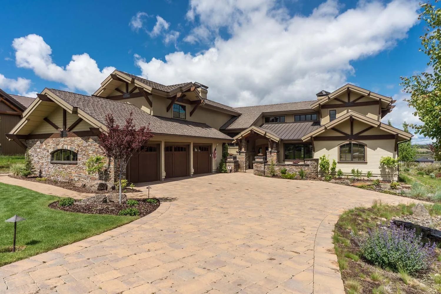 This stunning residence in Tetherow - Skene Trail, is a showcase of the masterful architecture design by Steve Van Sant. The large house features a striking stone and siding exterior, a three-car garage, and multiple gabled roofs. The beautifully lan