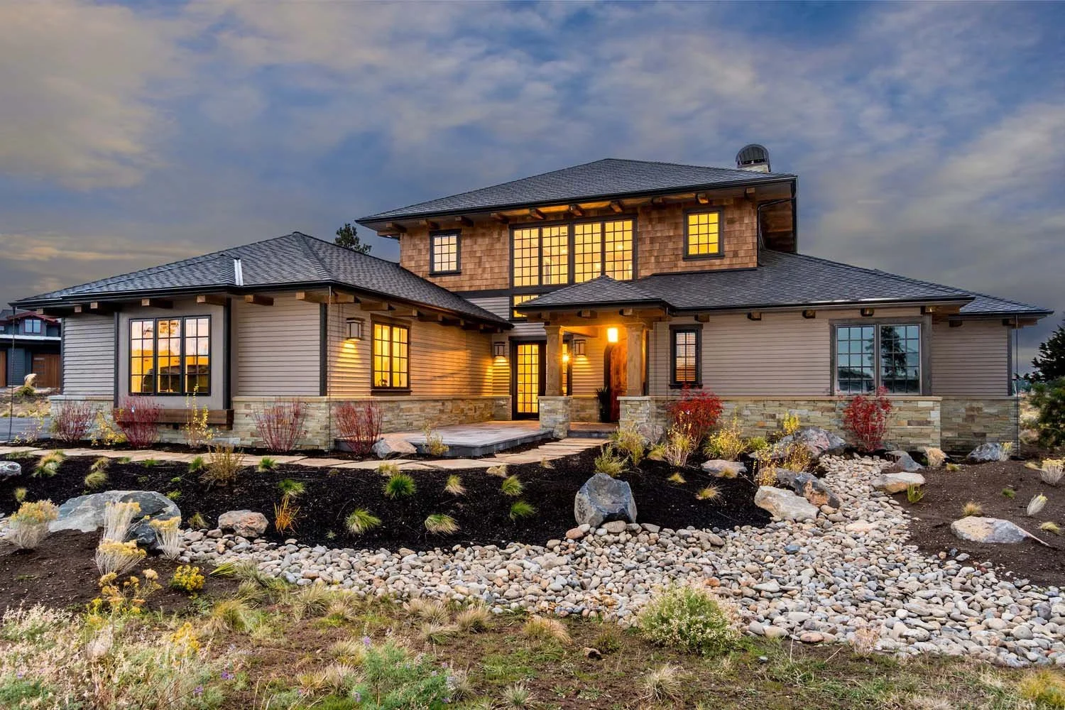 This luxury custom home in Tetherow - Skene Trail, design by Steve
Van Sant and built by Pacwest Builders, showcases stunning modern architecture. The two-story house features large windows and is surrounded by a beautifully landscaped yard with rock