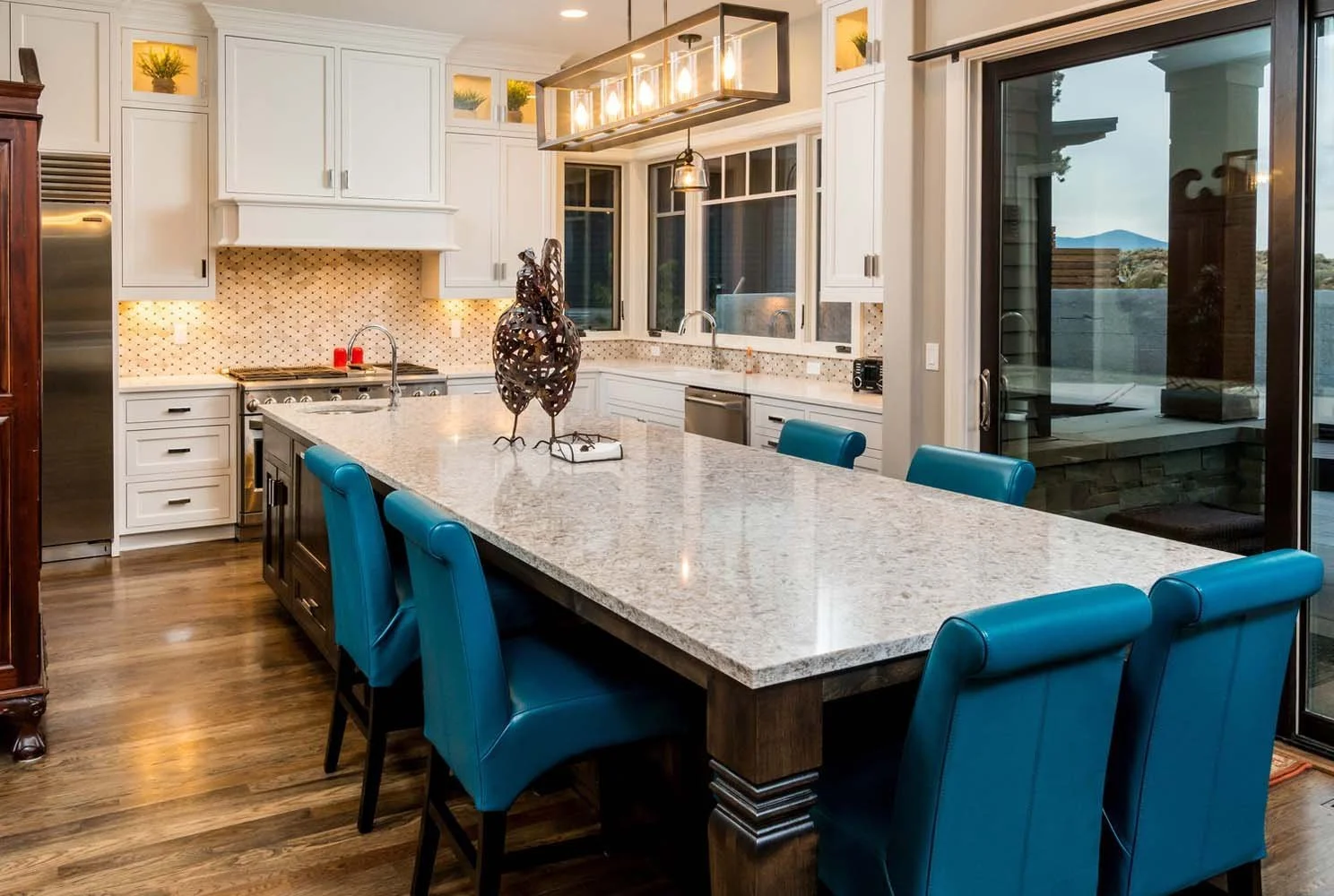 This cozy modern dining room in Tetherow - Skene Trail, a luxury custom home, is a beautiful showcase of interior design by Kristy Yozamp. The space, which flows seamlessly into a kitchen with white cabinets and a granite island, is furnished with a