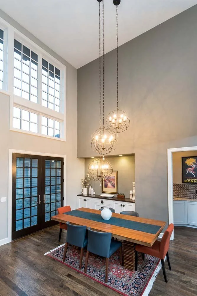 Discover the captivating interior design of this modern dining room in Tetherow - Skene Trail. The space features a large wooden table with colorful chairs and a built-in sideboard. The high vaulted ceiling and French doors that lead outside highligh