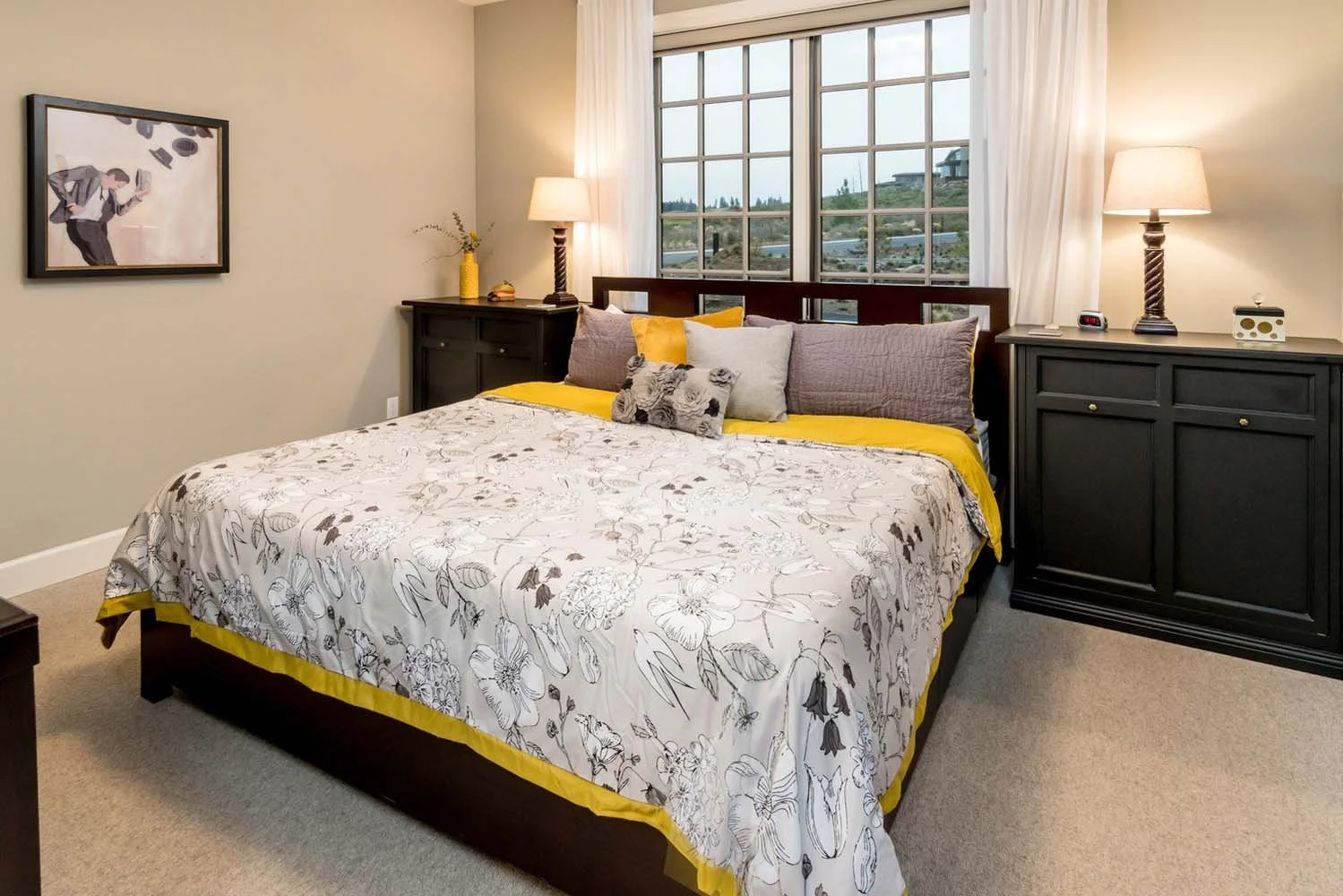 This bedroom in Tetherow - Skene Trail, a luxury custom home, is a beautiful showcase of interior design by Kristy Yozamp. The space, with its floral-patterned quilt and decorative pillows, has a welcoming feel. The use of a yellow bedspread adds a c