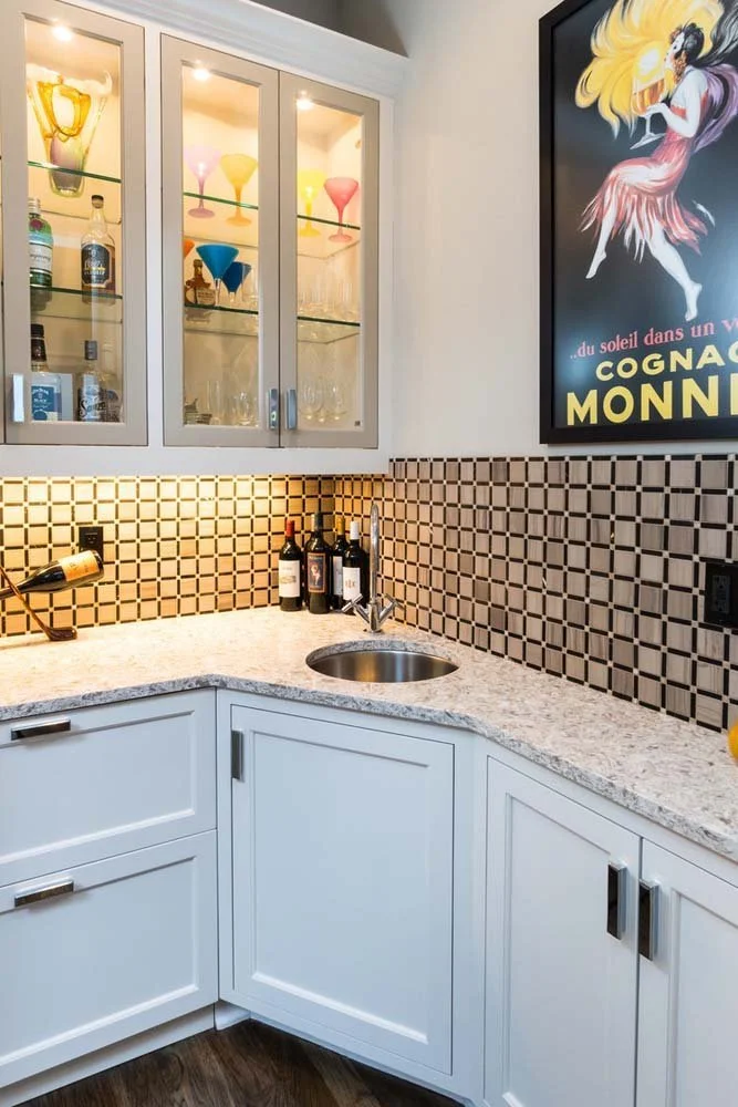 A beautiful showcase of interior design by Kristy Yozamp, this bar corner adds a inviting touch to this luxury custom home in Tetherow - Skene Trail. The space features white cabinets, a granite countertop with a small sink, and a glass-front cabinet