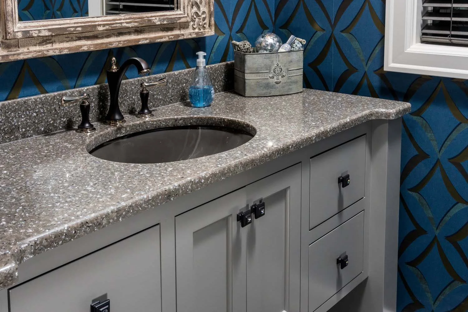 This bathroom vanity in Tetherow - Skene Trail, a luxury custom home, is a beautiful showcase of interior design by Kristy Yozamp. The space features a granite countertop with a black faucet, and a beautiful blue patterned wallpaper, perfectly blendi