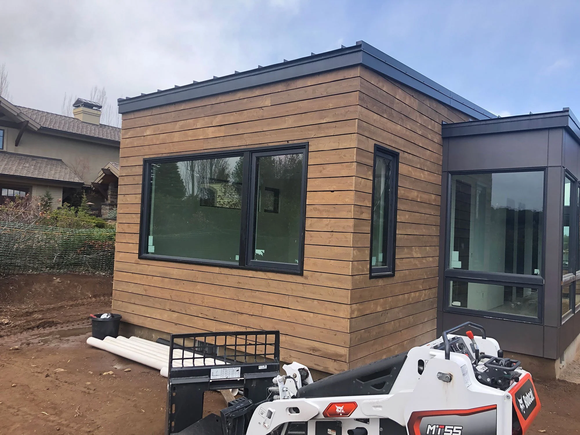 A modern house with a wooden exterior and large glass windows in a residential area under construction.