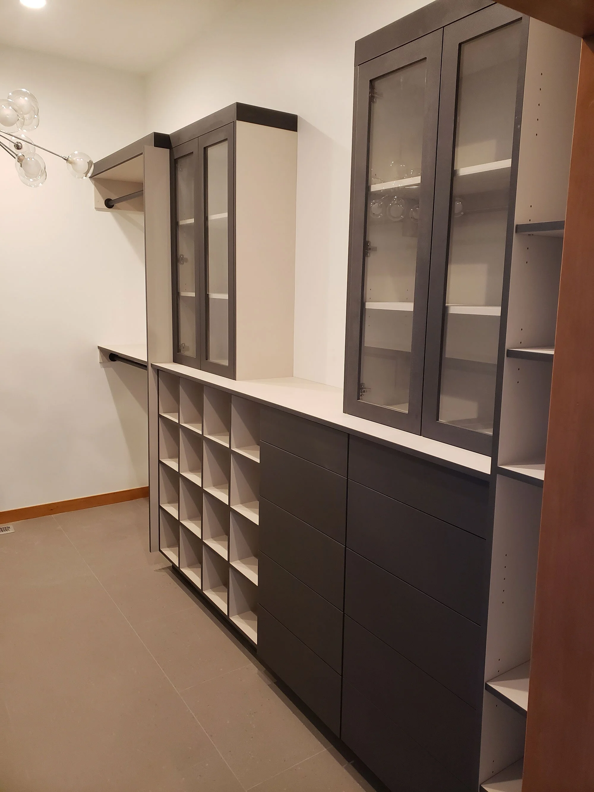 Modern kitchen cabinet with glass-front doors and open shelves, featuring a mix of dark and light gray finishes.