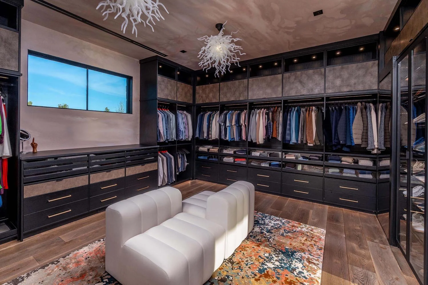 This impressive walk-in closet at the Pacific Cascade Heights home is a perfect blend of style and organization, a testament to the masterful interior design by Kate Darden. A stunning modern art light fixture provides a unique centerpiece, while cus