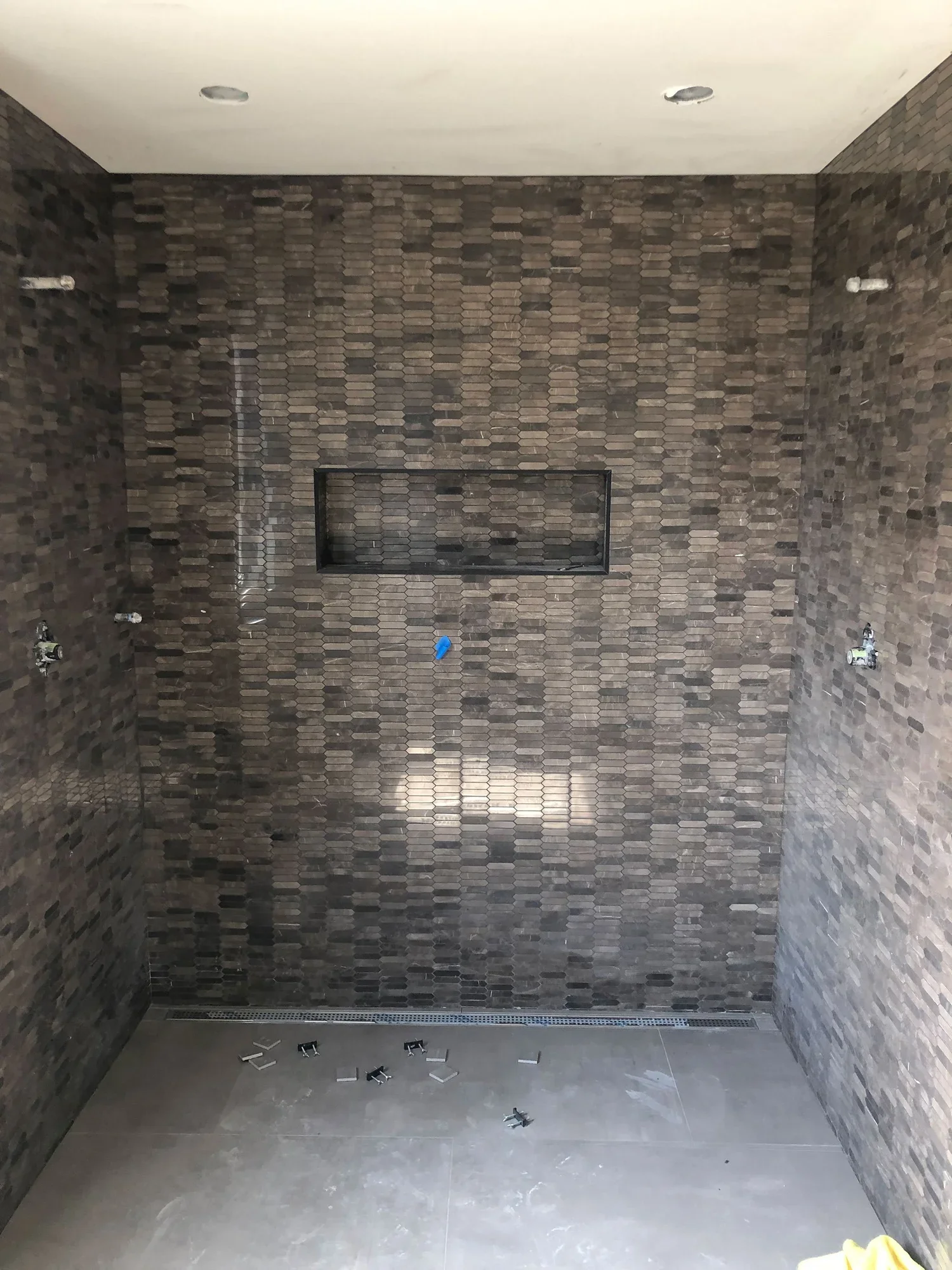 View of a bathroom shower area with dark tile walls, a niche in the wall, and construction materials on the floor.