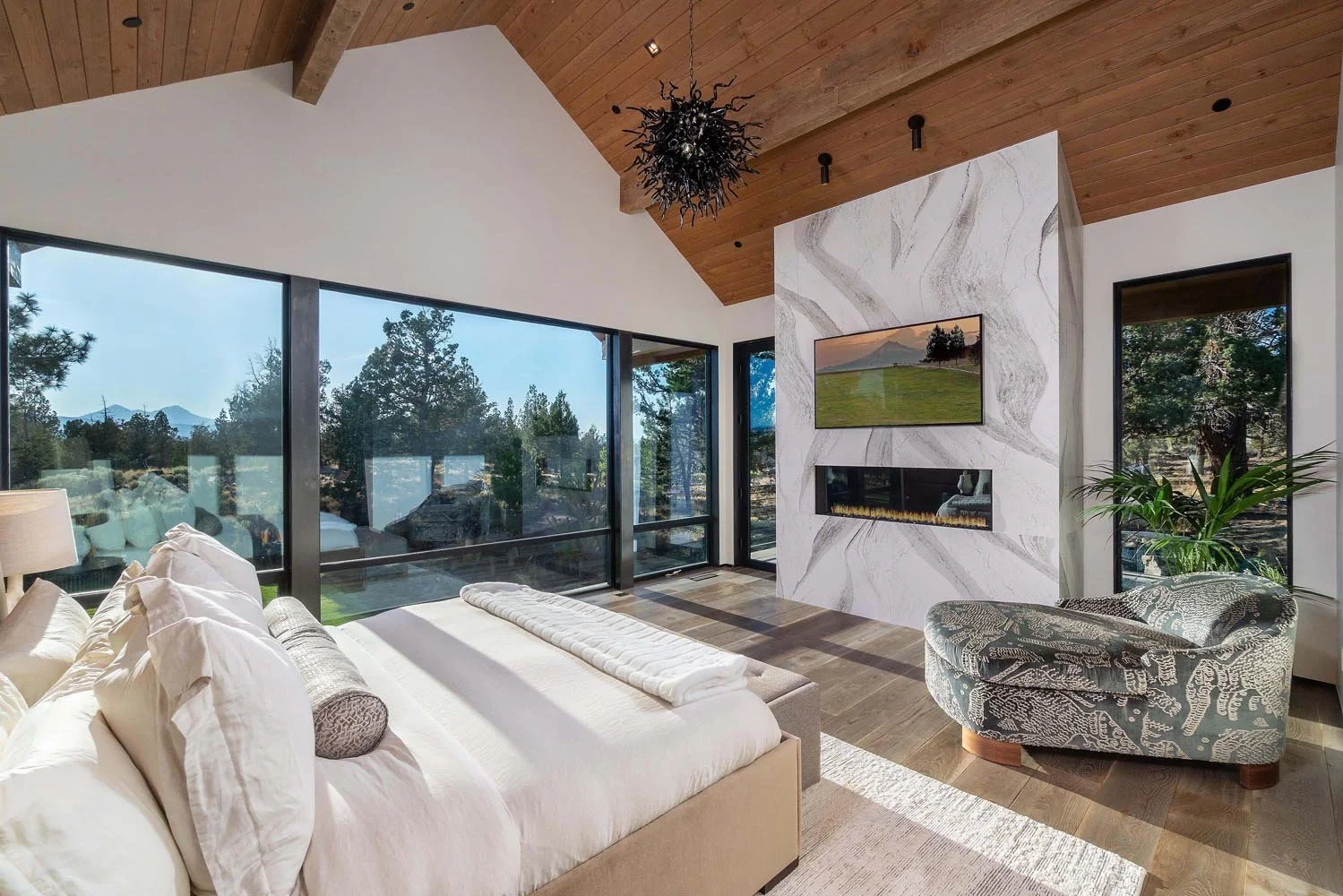This breathtaking modern master bedroom is a serene retreat within the Pacific Cascade Heights home in Central Oregon, showcasing Pacwest Builders' expertise in mountain modern design. A dramatic wooden vaulted ceiling with custom beams from Beamwork