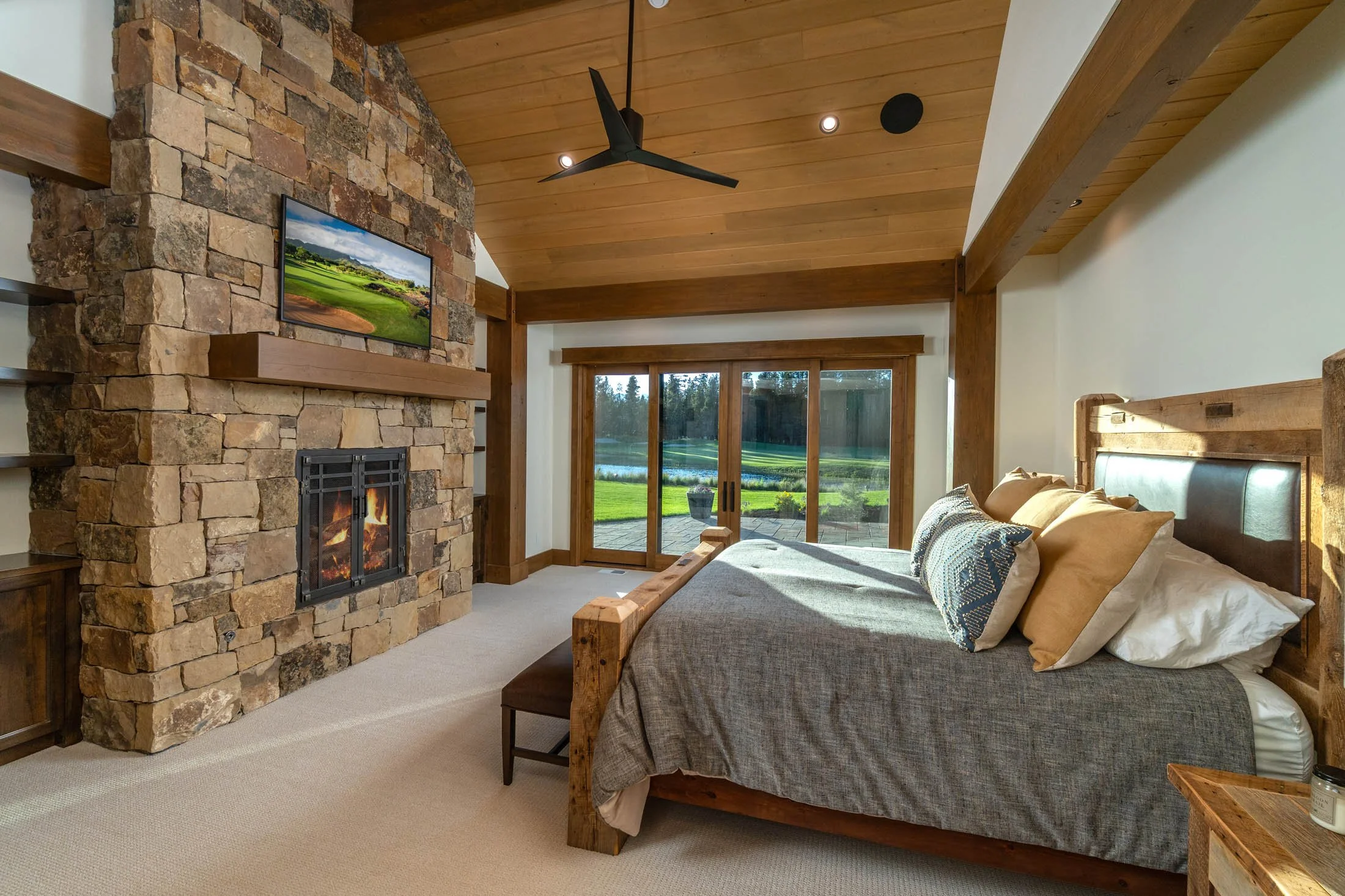 Cozy modern bedroom with a stone fireplace and wood-beamed ceiling in a Crosswater custom home by Bend Oregon builder Pacwest Builders.