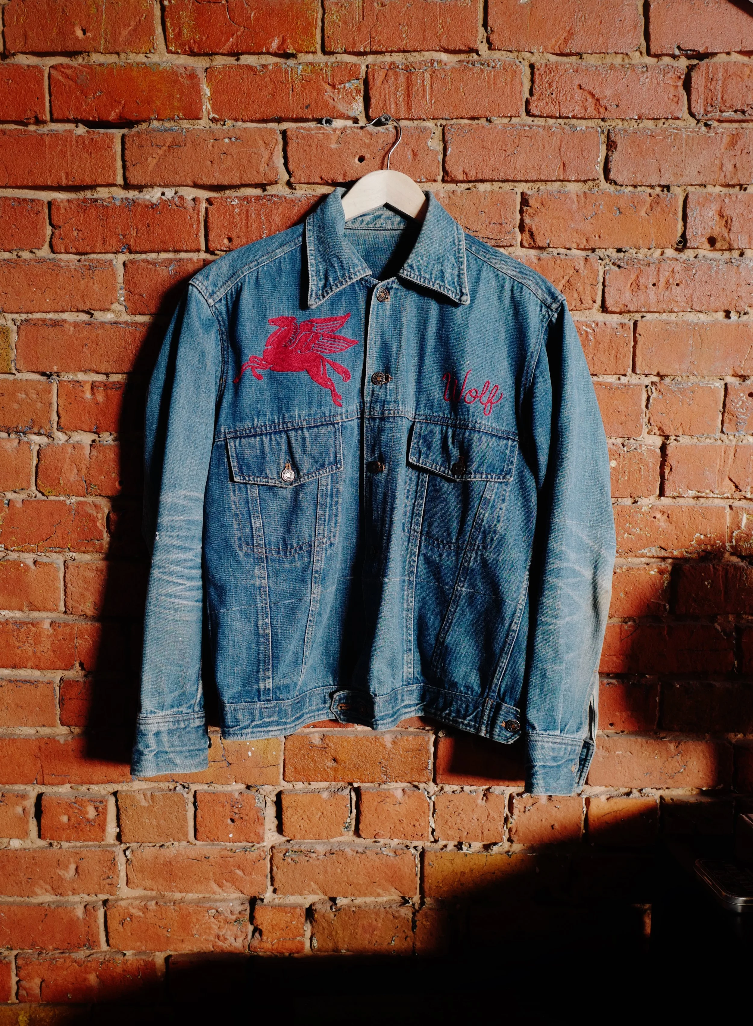 A custom hand cranked chainstitch embroidered  jacket that features an embroidered red Pegasus on the left chest area and the word 'Wolf' stitched in red on the right chest area. made in Dallas, Texas on a Cornely.
