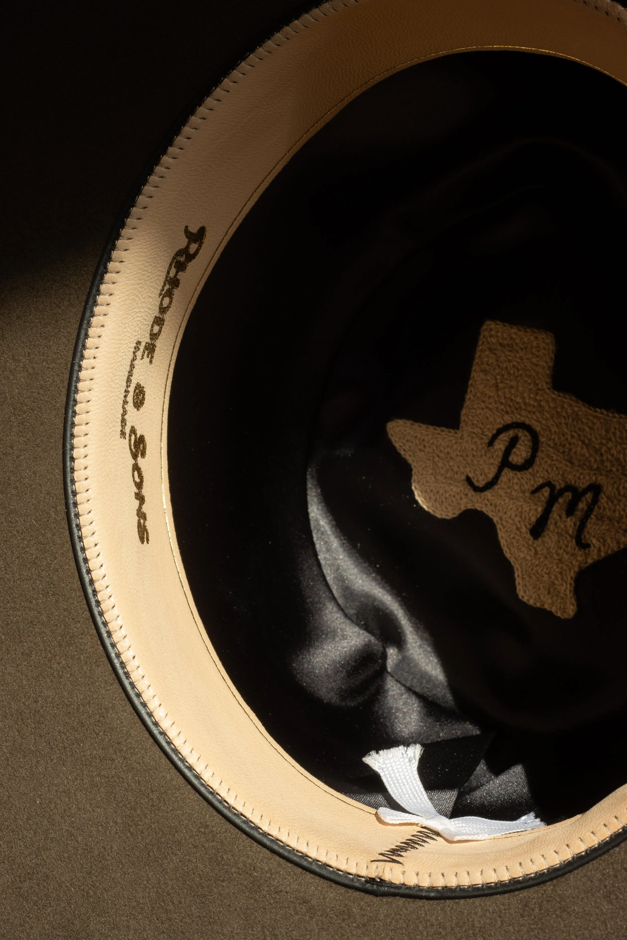 Interior of a custom made pure beaver hat featuring a sheepskin gold foil stamped sweatband, black silk liner and chainstitched Texas graphic with the customers initials. Made in a hat shop in Dallas Texas. 