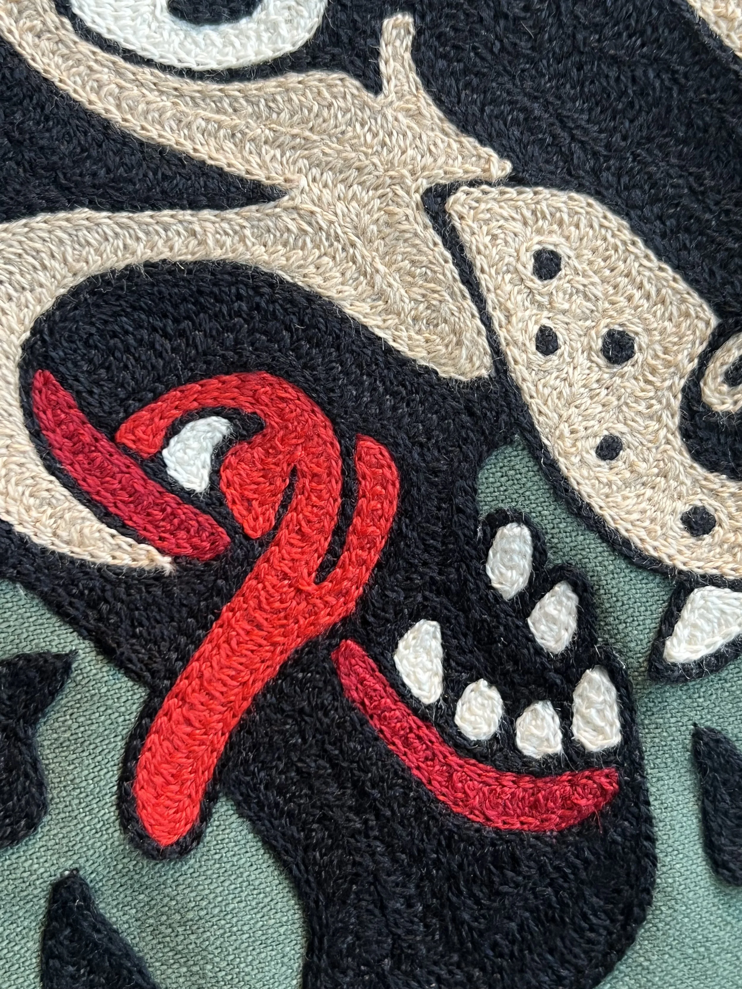 Close-up of embroidered patch featuring a red snake and a black dog with white teeth, on a background of black, beige, and green fabric.