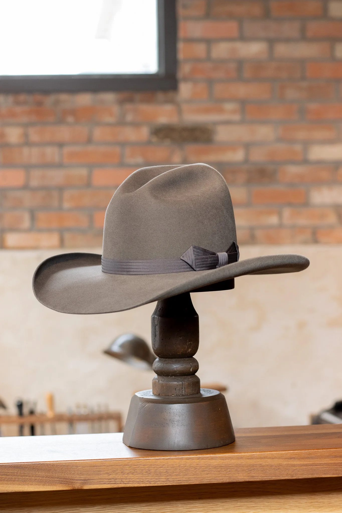 Gray fedora hat with a black ribbon and bow, displayed on a wooden stand.