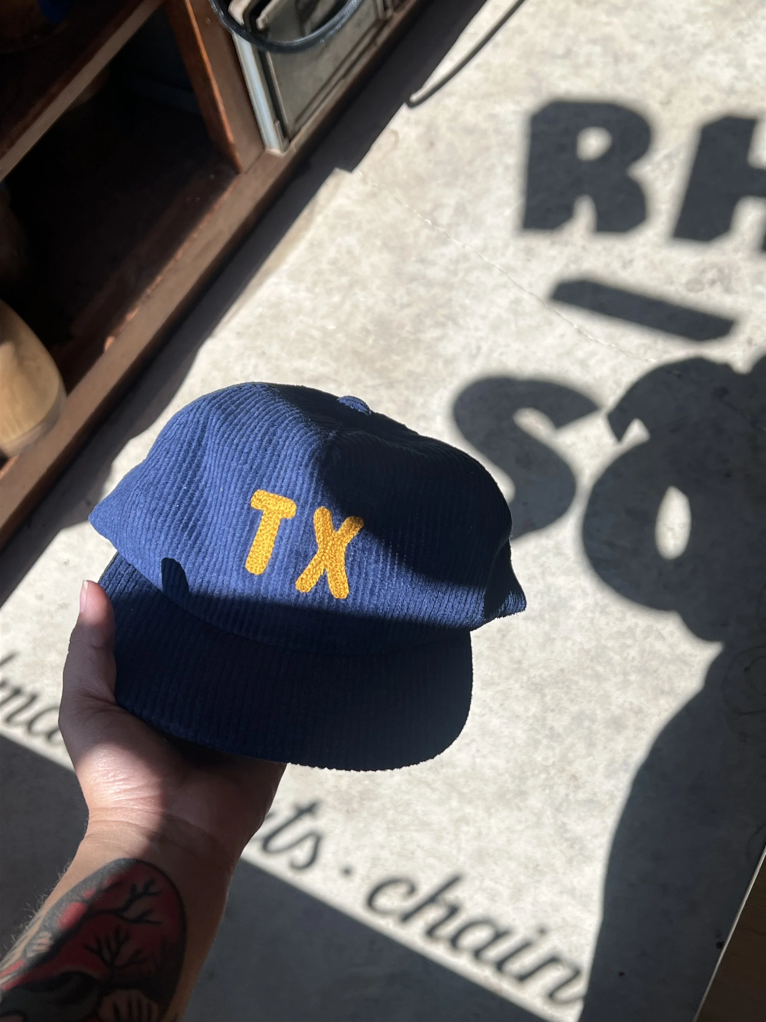 Hand holding a navy blue knit cap with yellow embroidered letters 'TX' on it.