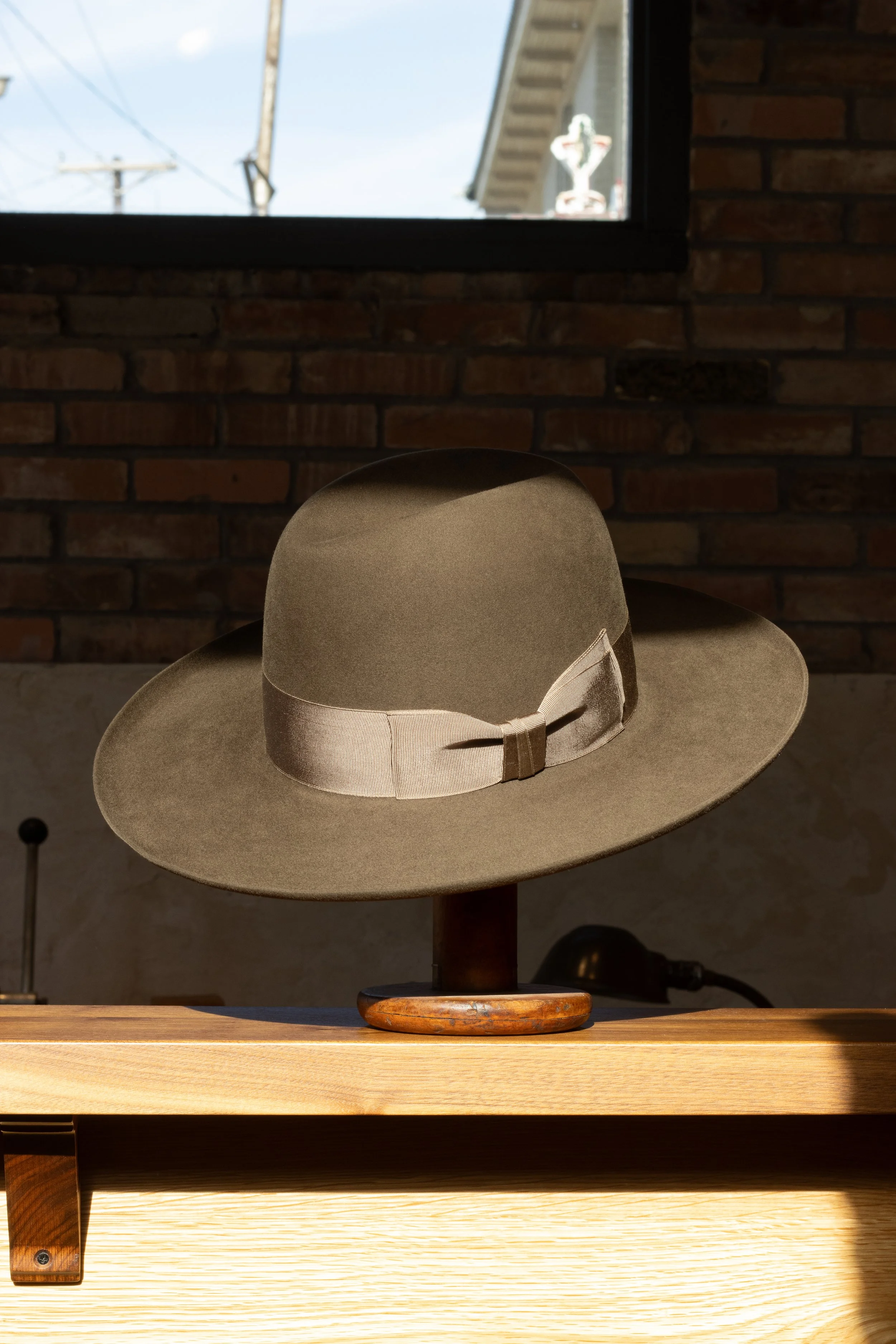 A gray brown center creased hat handmade in Dallas Texas by a custom hatter in a brick and mortar store. Using traditional grosgrain ribbon. Made using a conformateur and vermillion.