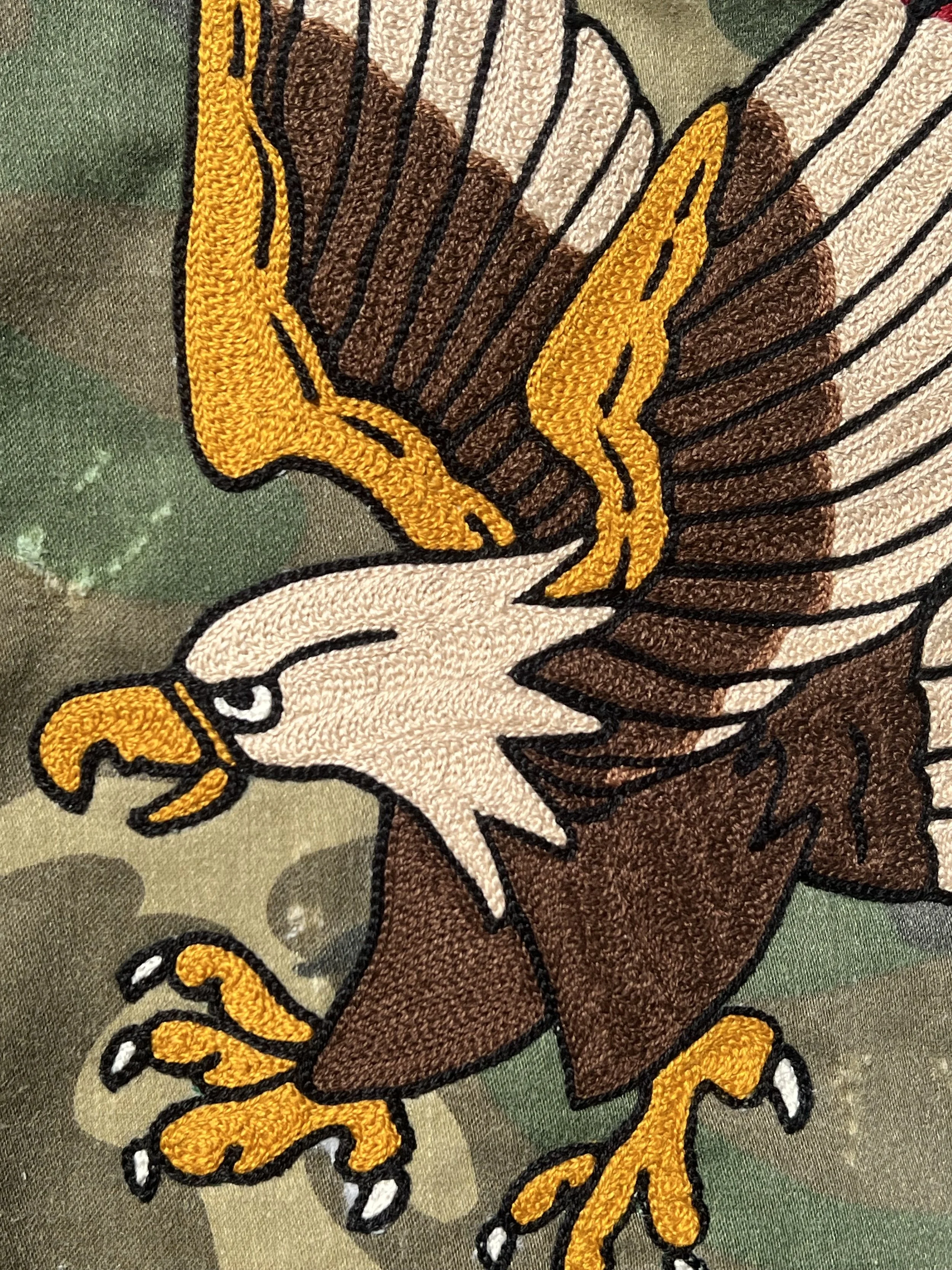 Close-up of an embroidered eagle with yellow beak and talons, white head, brown wings and body, on a green fabric background. the best chainstitch embroidery in Texas and specializes in live on site chainstitching