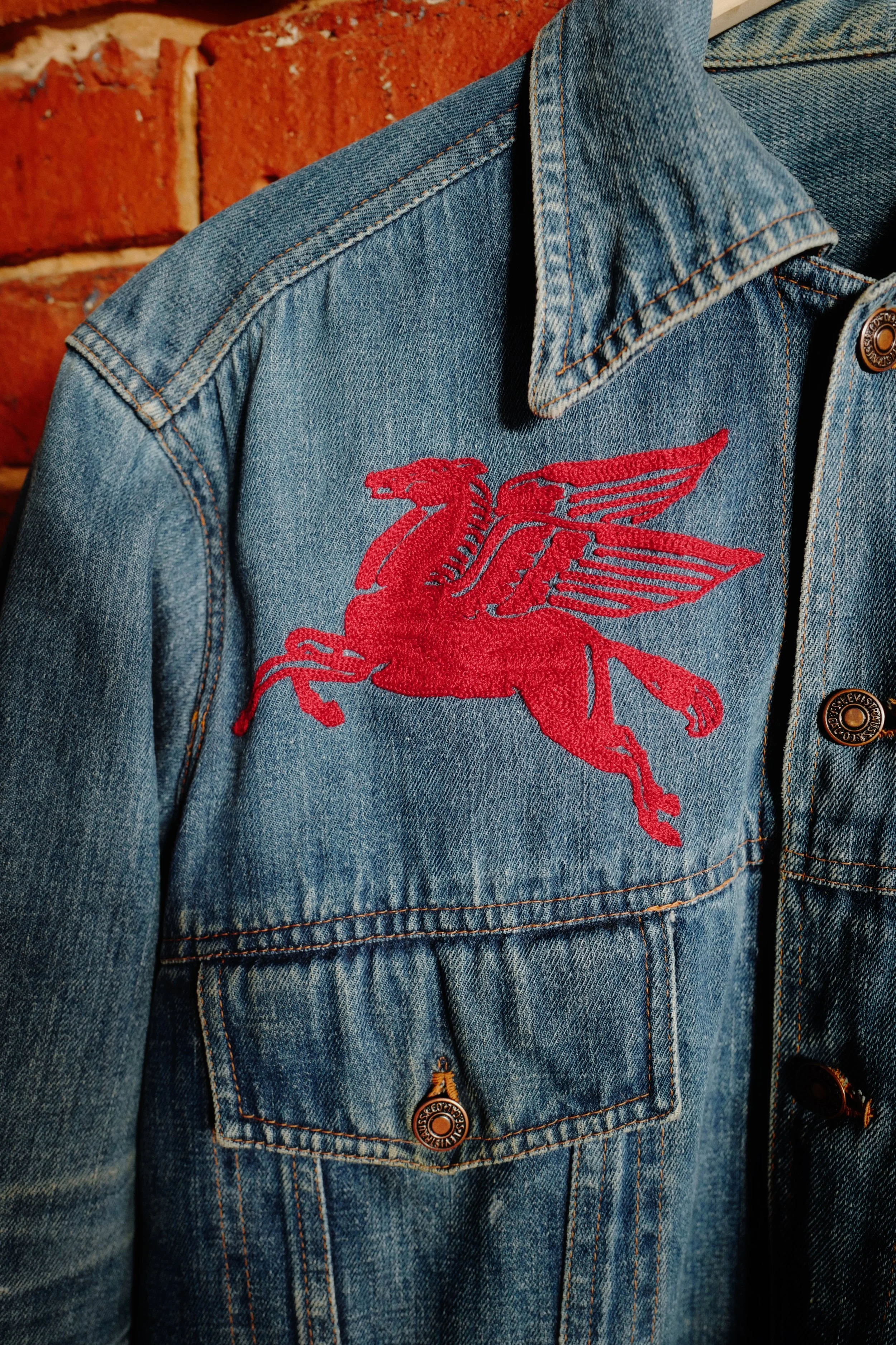 Selvedge Denim jacket with custom vintage style hand cranked chainstitch embroidery of a red Dallas pegasus. made in a store in Texas who provides custom chainstitch embroidery services. 