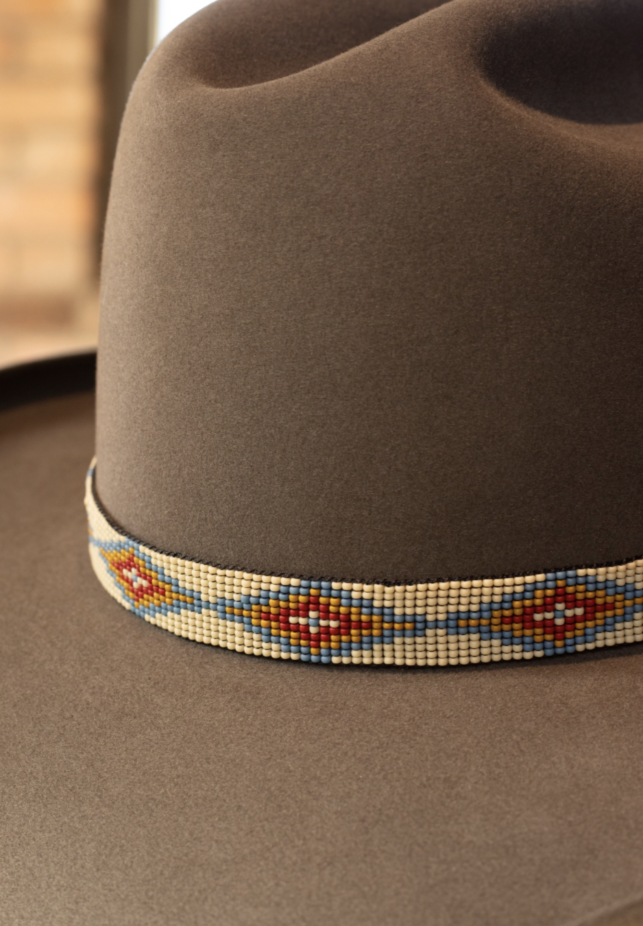 Close-up of a brown hat with a colorful beaded band featuring geometric patterns in red, yellow, blue, and white.