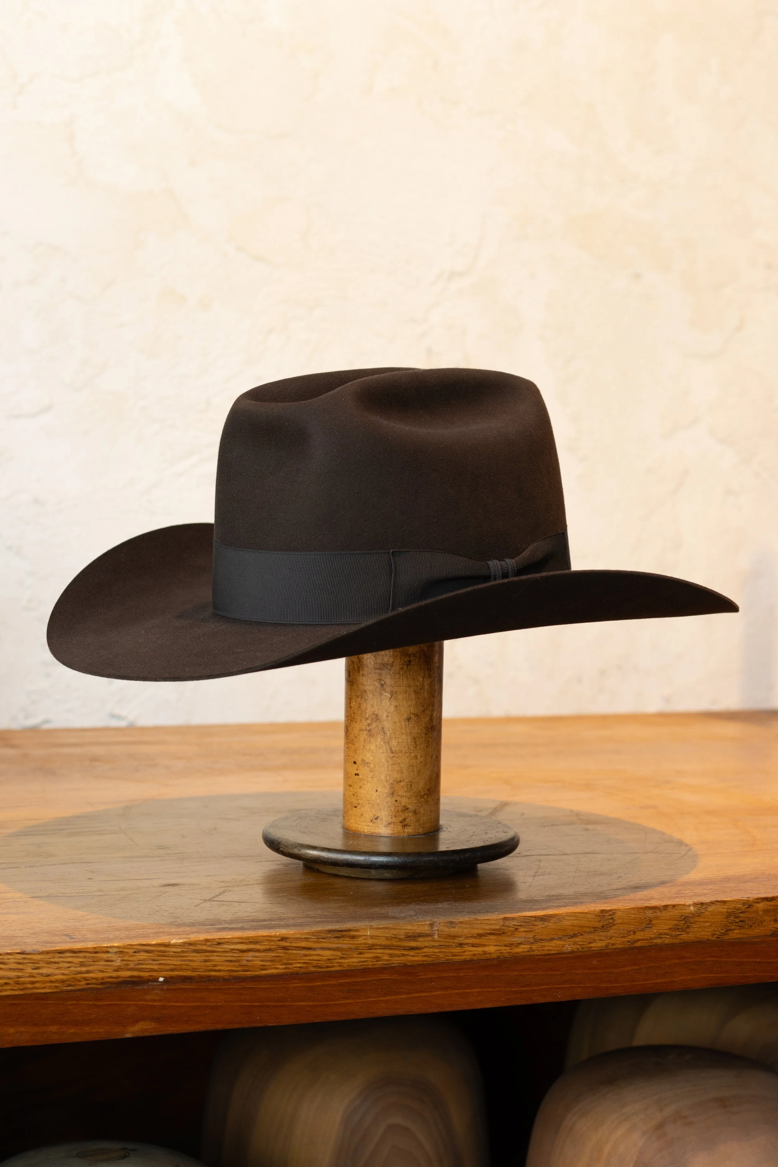 Black cowboy hat displayed on a wooden hat stand on a wooden surface.
