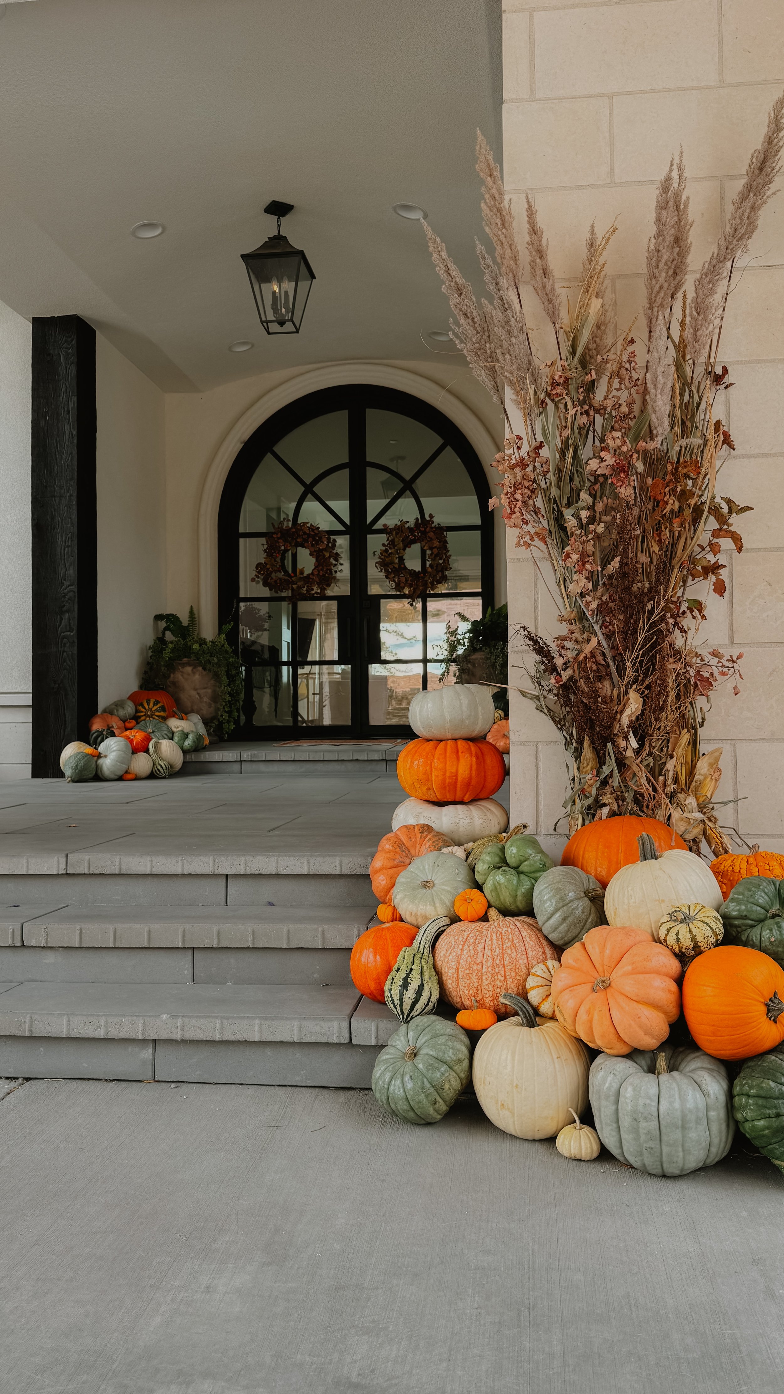 Porch Pumpkin display outside a house with various pumpkins and gourds, along with dried ornamental grasses, for fall or Halloween decoration. Professional Seasonal Stylist service for fall, christmas, halloween, and the holidays in Colorado.