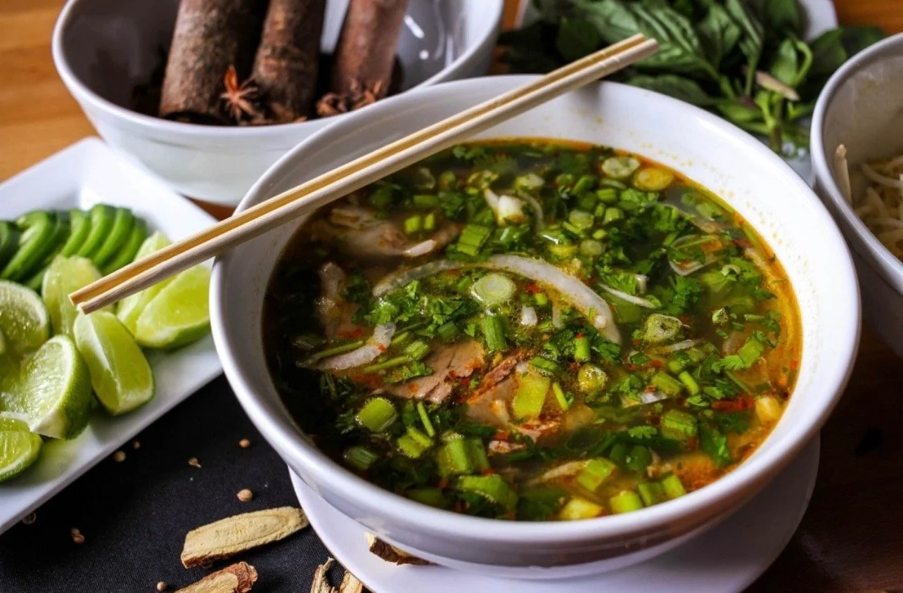 A bowl of Vietnamese Bun Bo Hue with beef and pork. Topped with herbs.