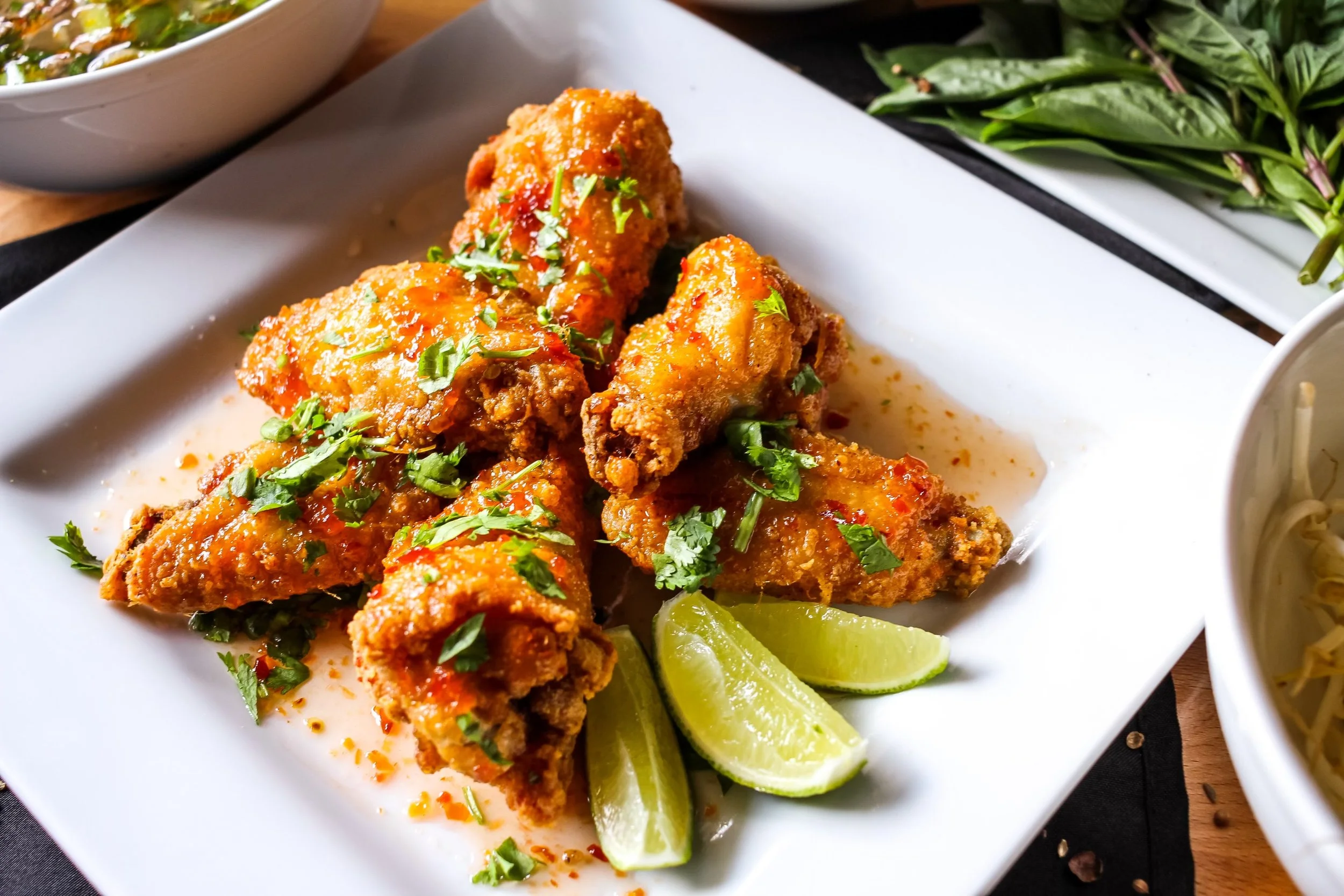 Fried chicken wings garnished with chopped cilantro and lime wedges on a white plate.