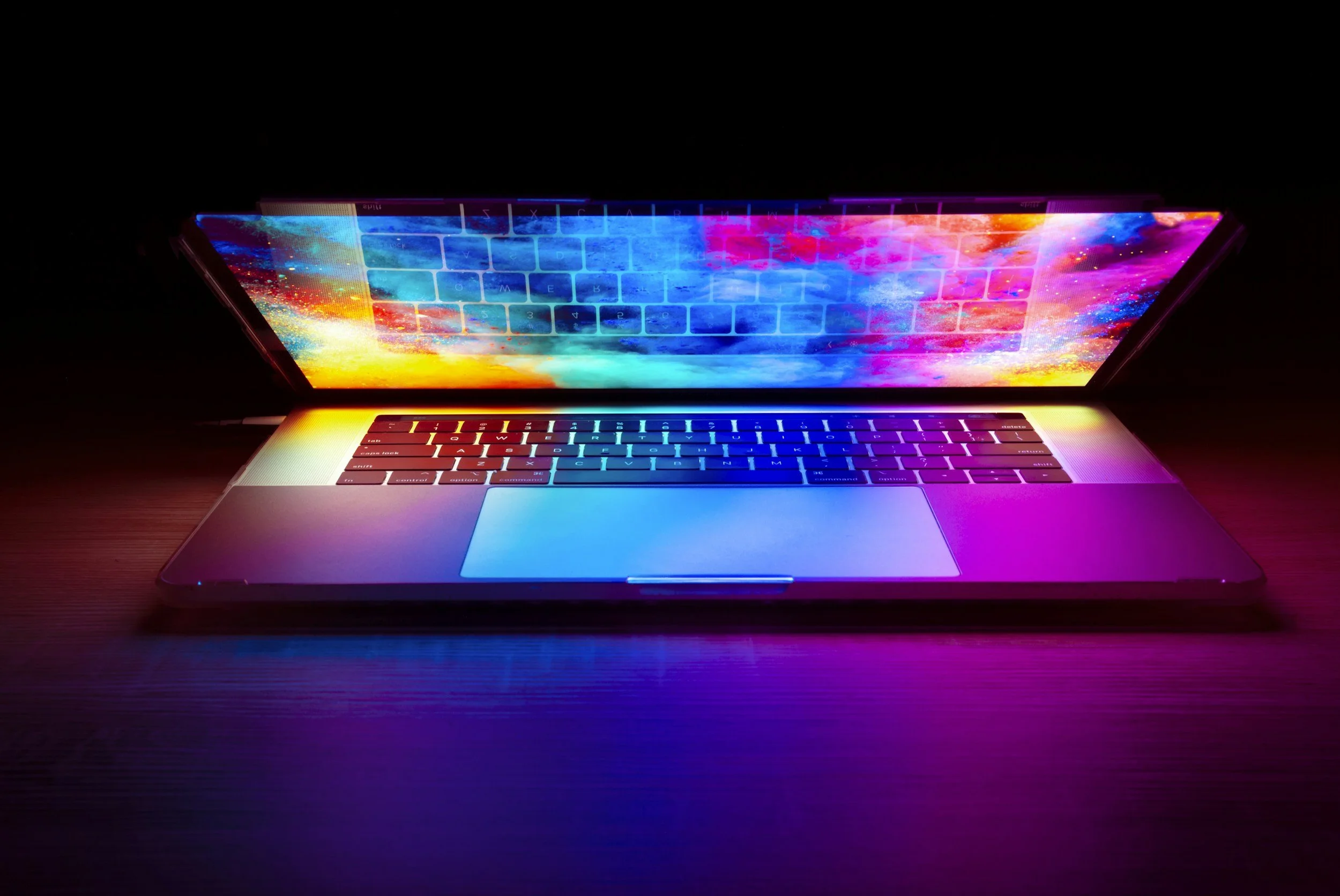 Laptop with illuminated screen displaying a colorful, abstract background reflecting on the dark surface beneath it.