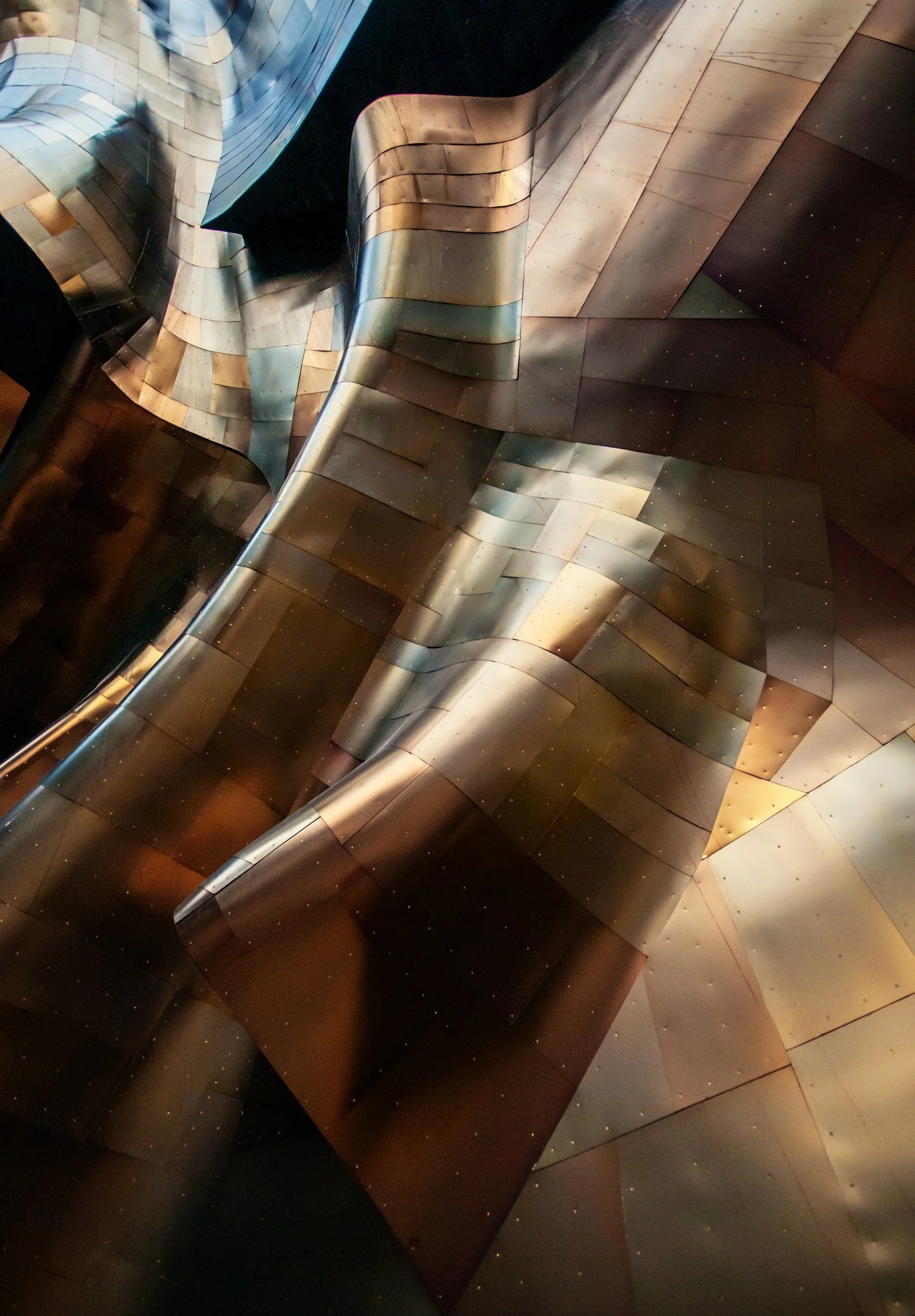 Close-up of a metallic, sculptural architectural structure with smooth, curving surfaces and a reflective metallic finish.