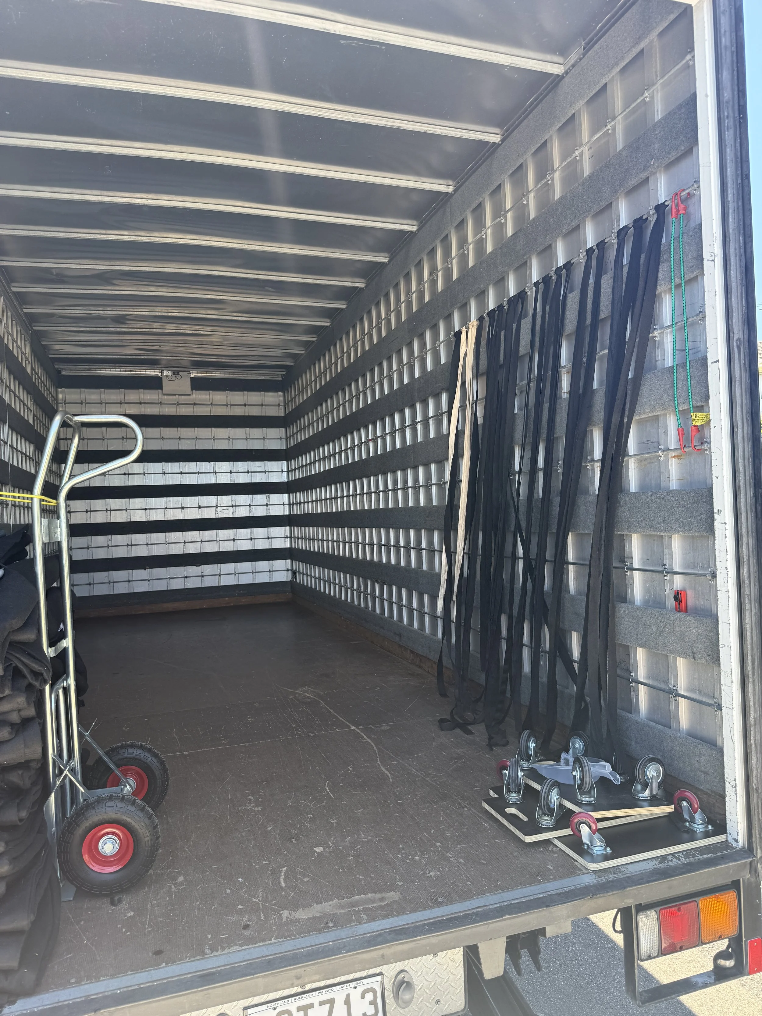 Empty moving truck with a hand truck, black straps hanging on the side, and roller skates on the floor.