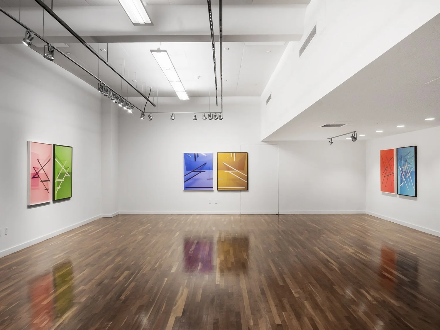 An art gallery with white walls and hardwood floors displaying colorful abstract paintings.