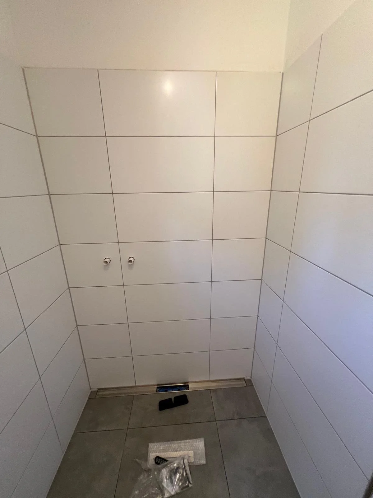 Ein neues, weiß gekacheltes Badezimmer ohne Armaturen, mit Installationsöffnungen an den Wänden, bereit für die Montage von Sanitäranlagen.