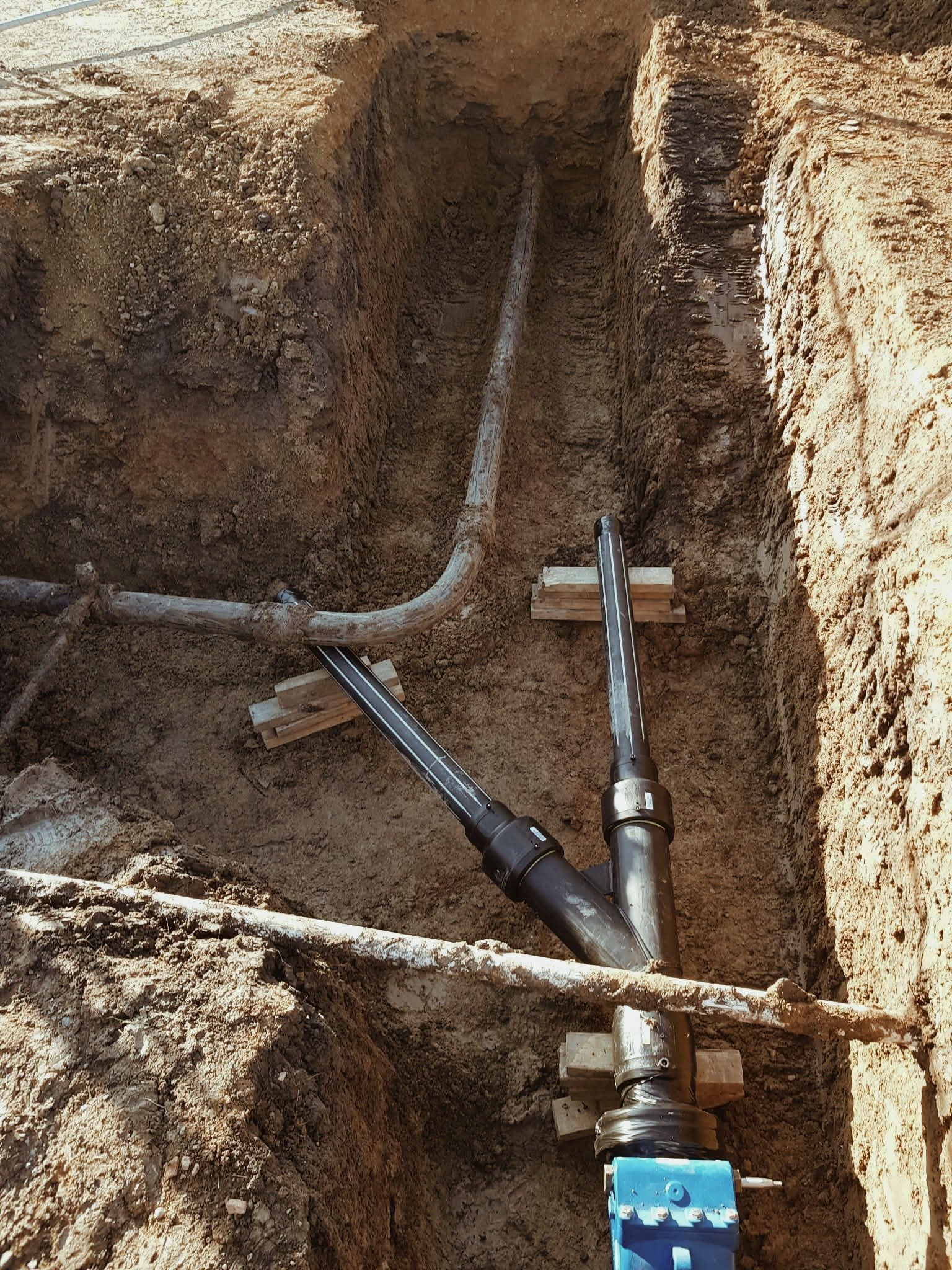 Steel pipes installed in a trench for underground utility lines, supported by wooden blocks.