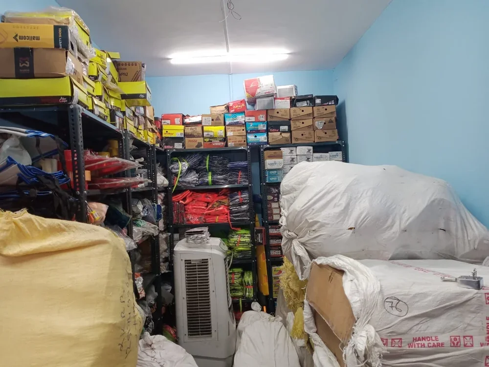 Storage room filled with shelves of various boxes, bags, and equipment, along with large bags and an air conditioning unit.