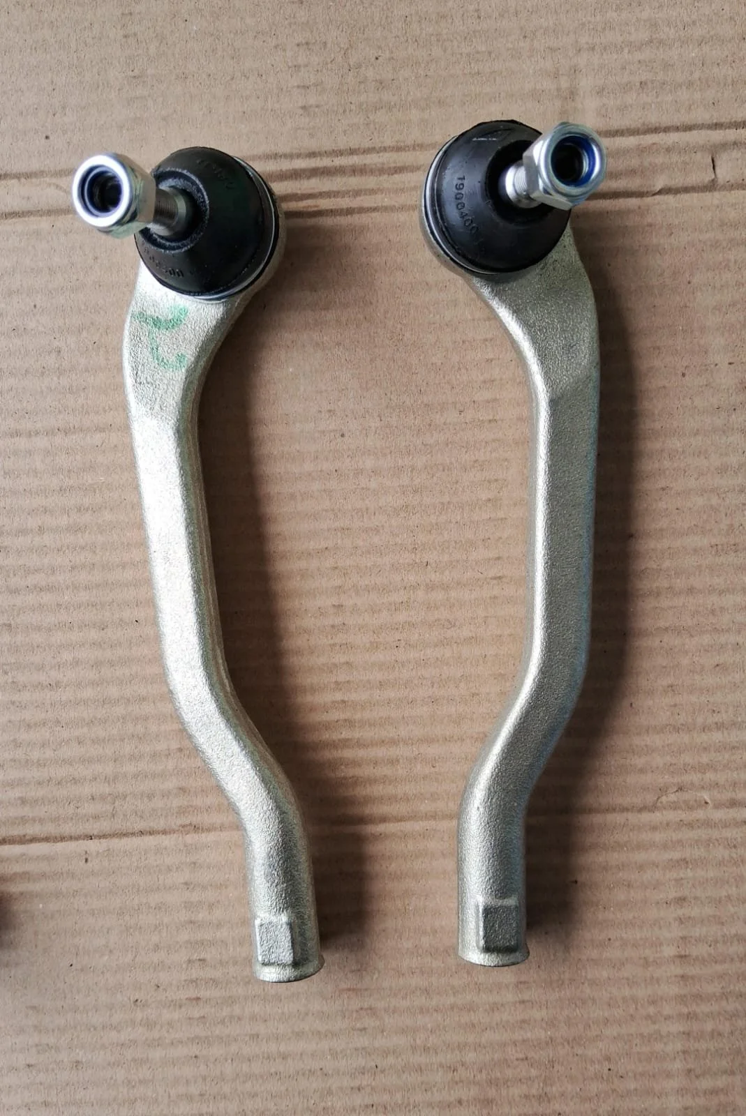Two metal control arms with black ball joints, placed on a cardboard surface.