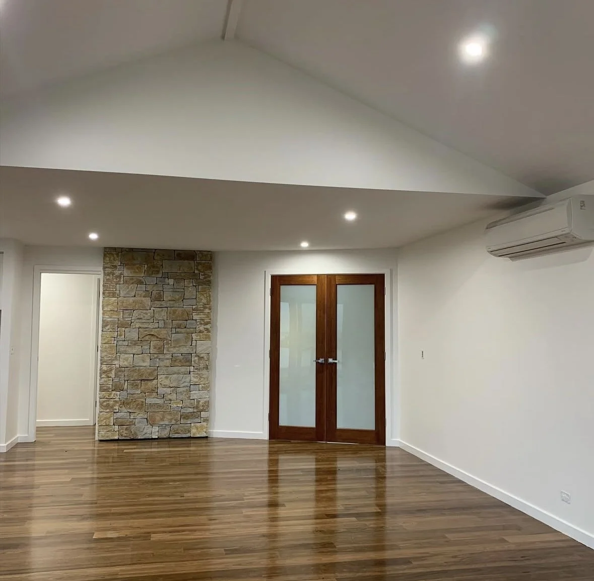 newly painted interior of an empty room with wooden floors, white walls, a stone accent wall, and a set of wooden double doors with frosted glass panes.