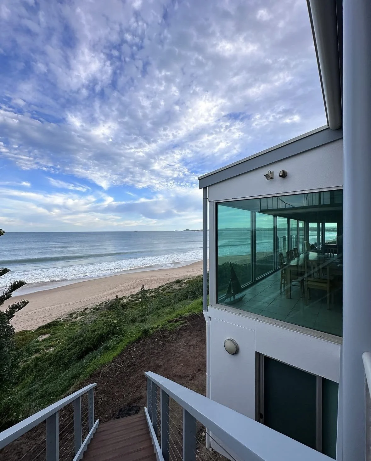 repainted house View of a beach with waves and clouds in the sky, seen from a house with large glass windows reflecting the sea.