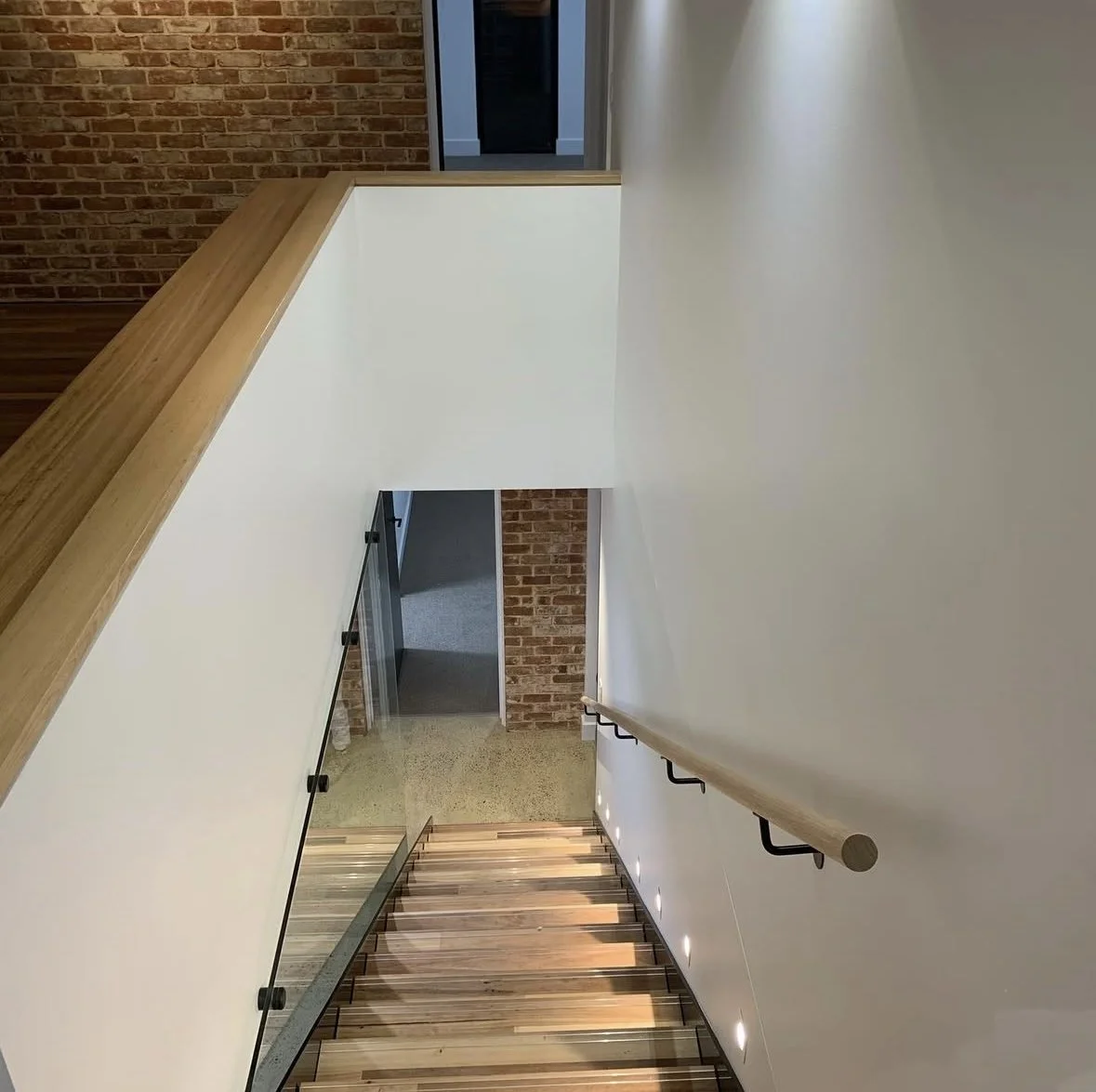painted Interior view of a modern staircase with wooden steps, glass railing, a white wall, and a brick wall in the background.