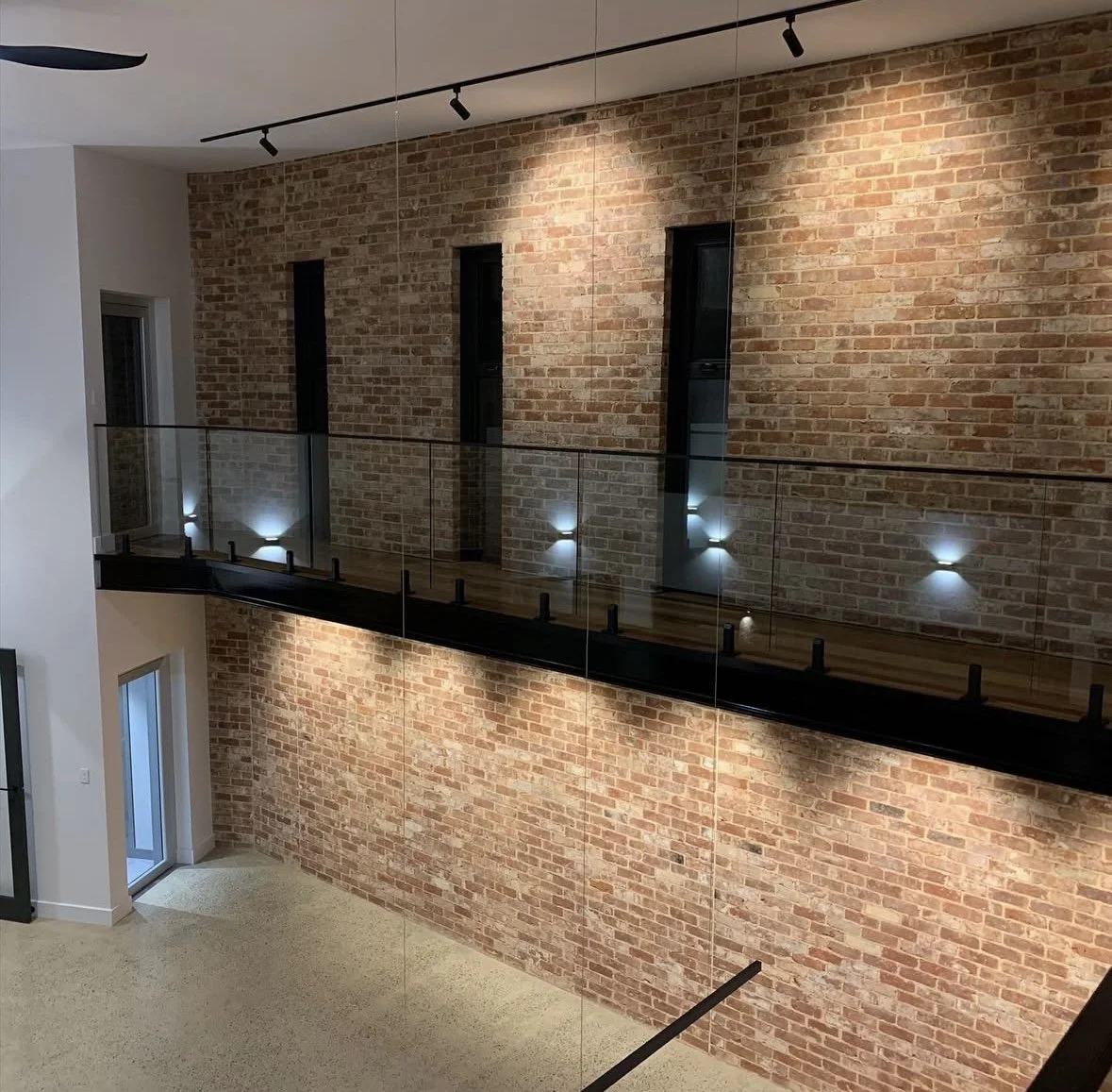 freshly painted Interior view of a modern building with brick walls, a glass balcony with metal supports, and small wall-mounted lights.